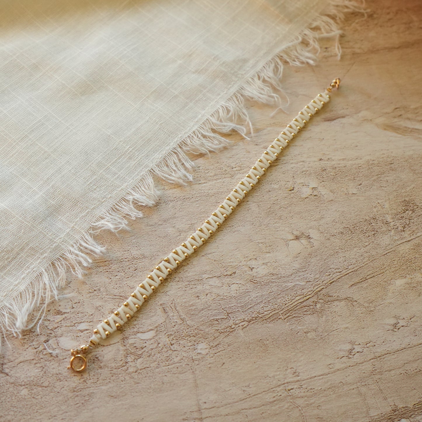 unclasped bracelet with white Japanese glass and gold-fill ball beads next to a white cloth
