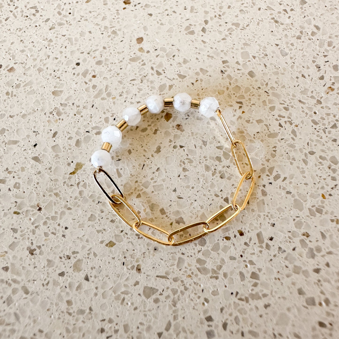 close up of ring with white moonstone faceted quartz stones and gold-filled chain n a quartz countertop