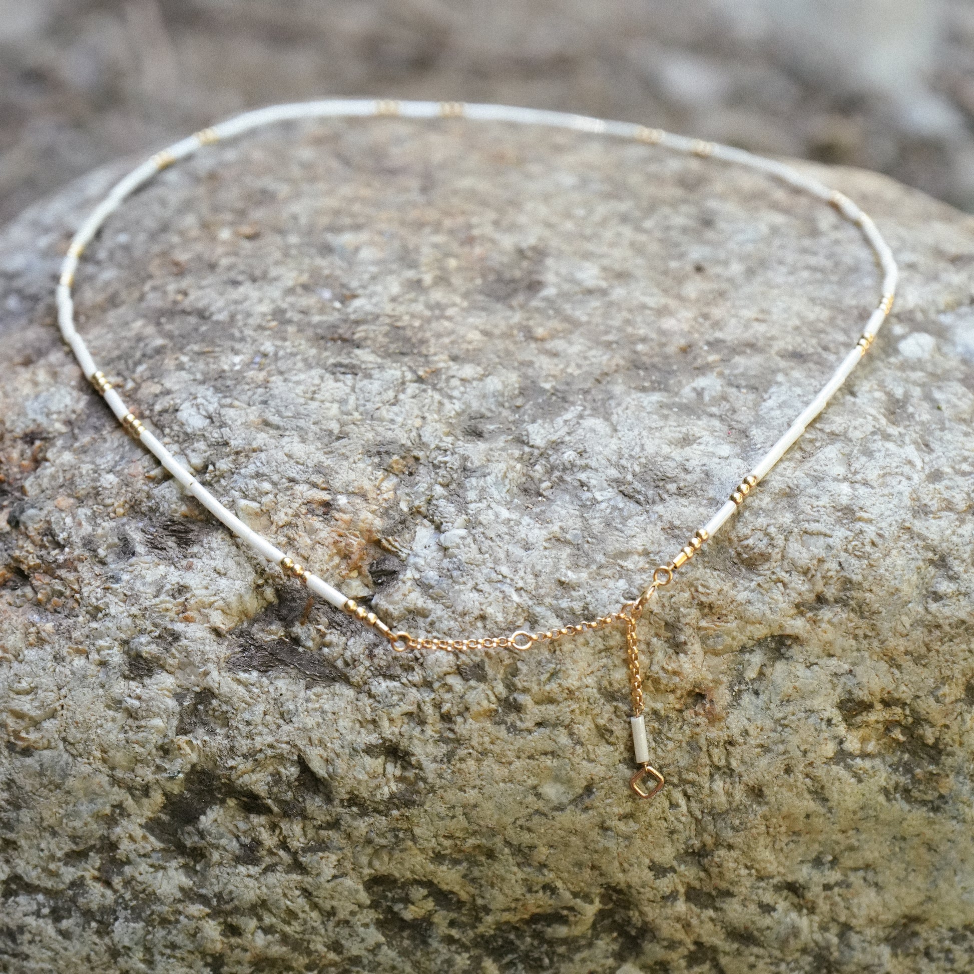 white and gold beaded necklace with a dangling extension chain at the clasp