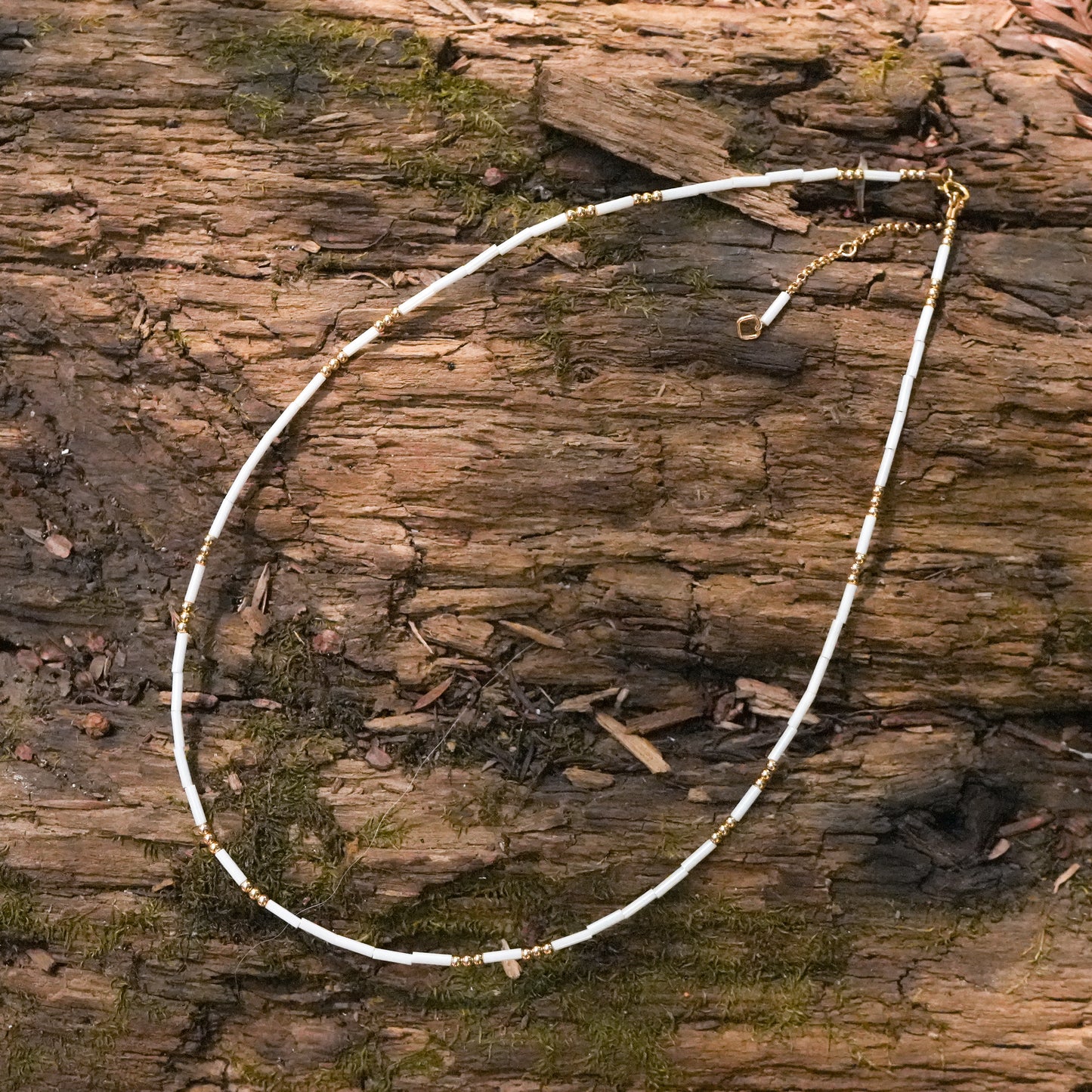 white and gold beaded necklace on wood surface