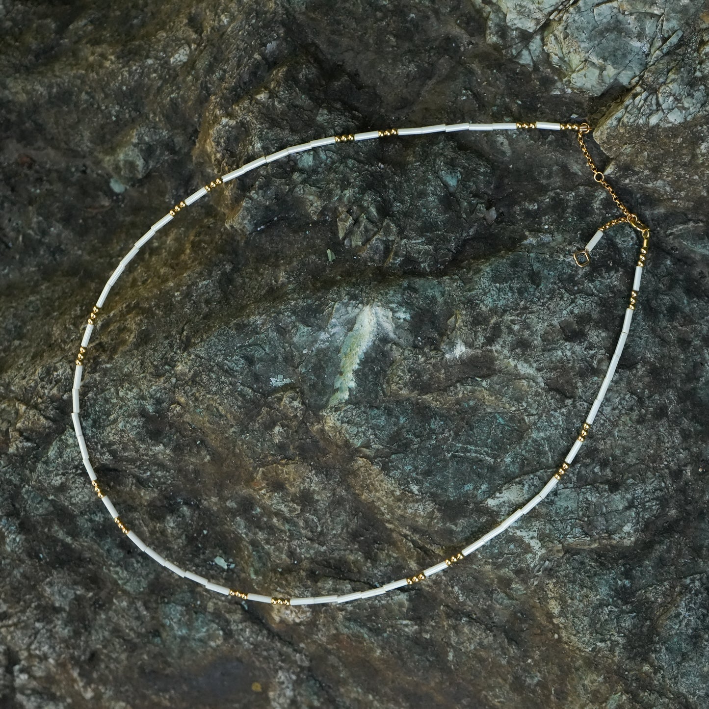 white and gold beaded necklace on a stone