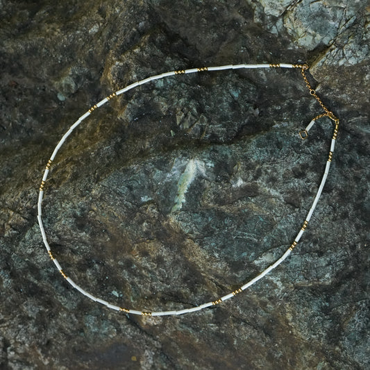 white and gold beaded necklace on a stone