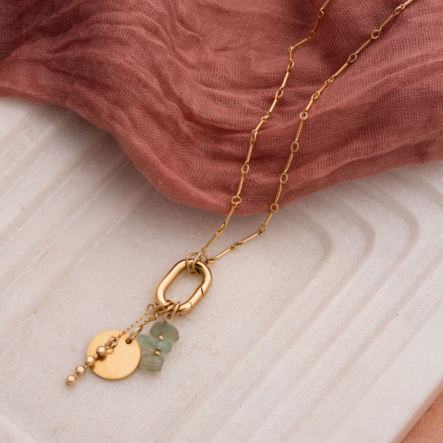 gold-filled necklace with raw Ecuadorian jade stones and gold charms on a marble tray