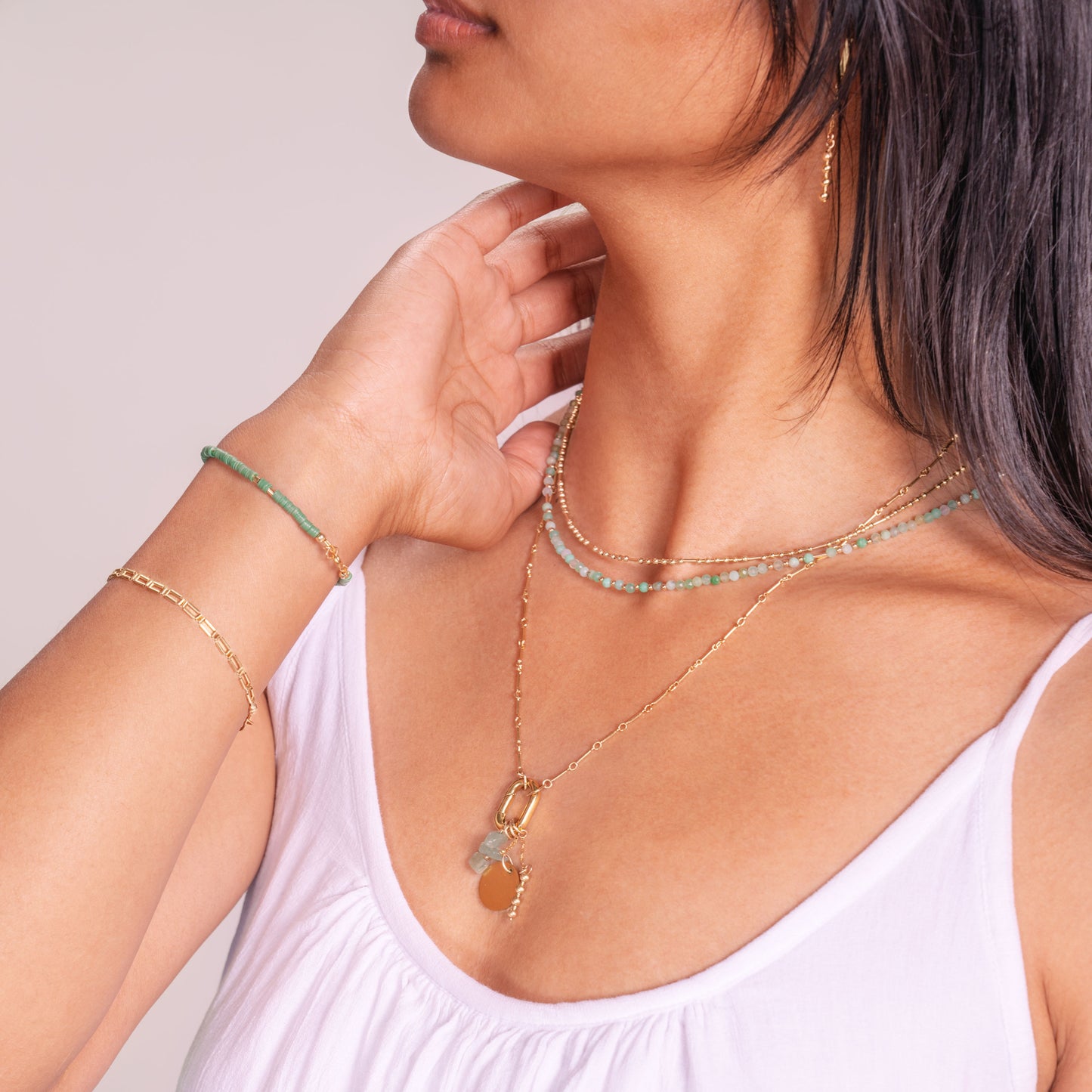 woman wearing gold-filled necklaces and bracelets containing jade, vinyl heishi beads, and chrysoprase faceted stones