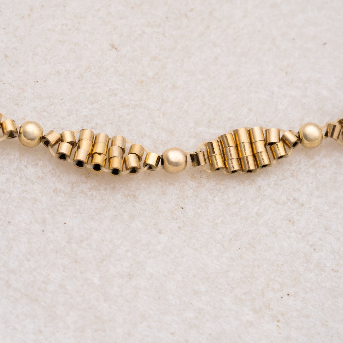 close up view of gold-filled cylindrical and spherical beads in a double-helix pattern