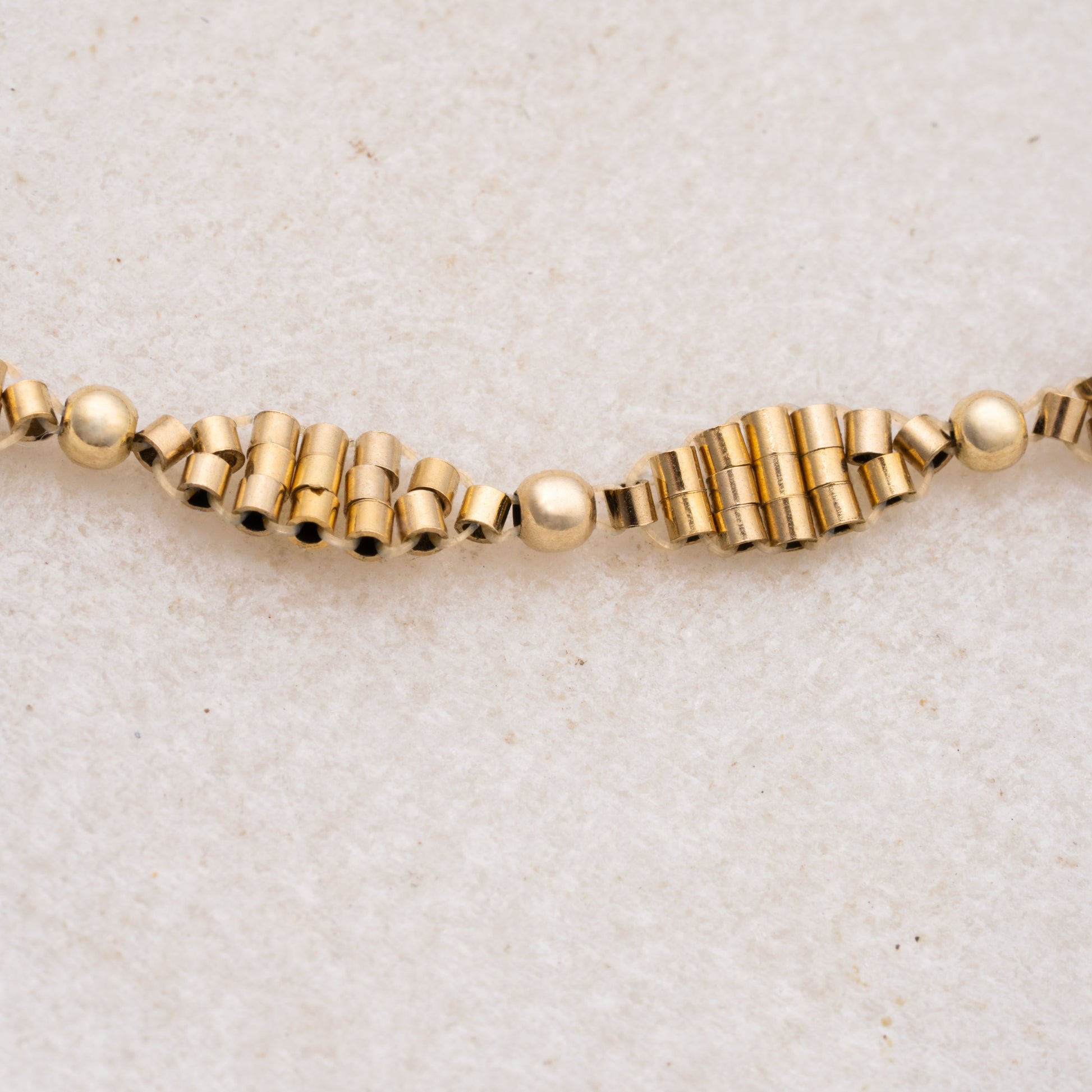 close up view of gold-filled cylindrical and spherical beads in a double-helix pattern