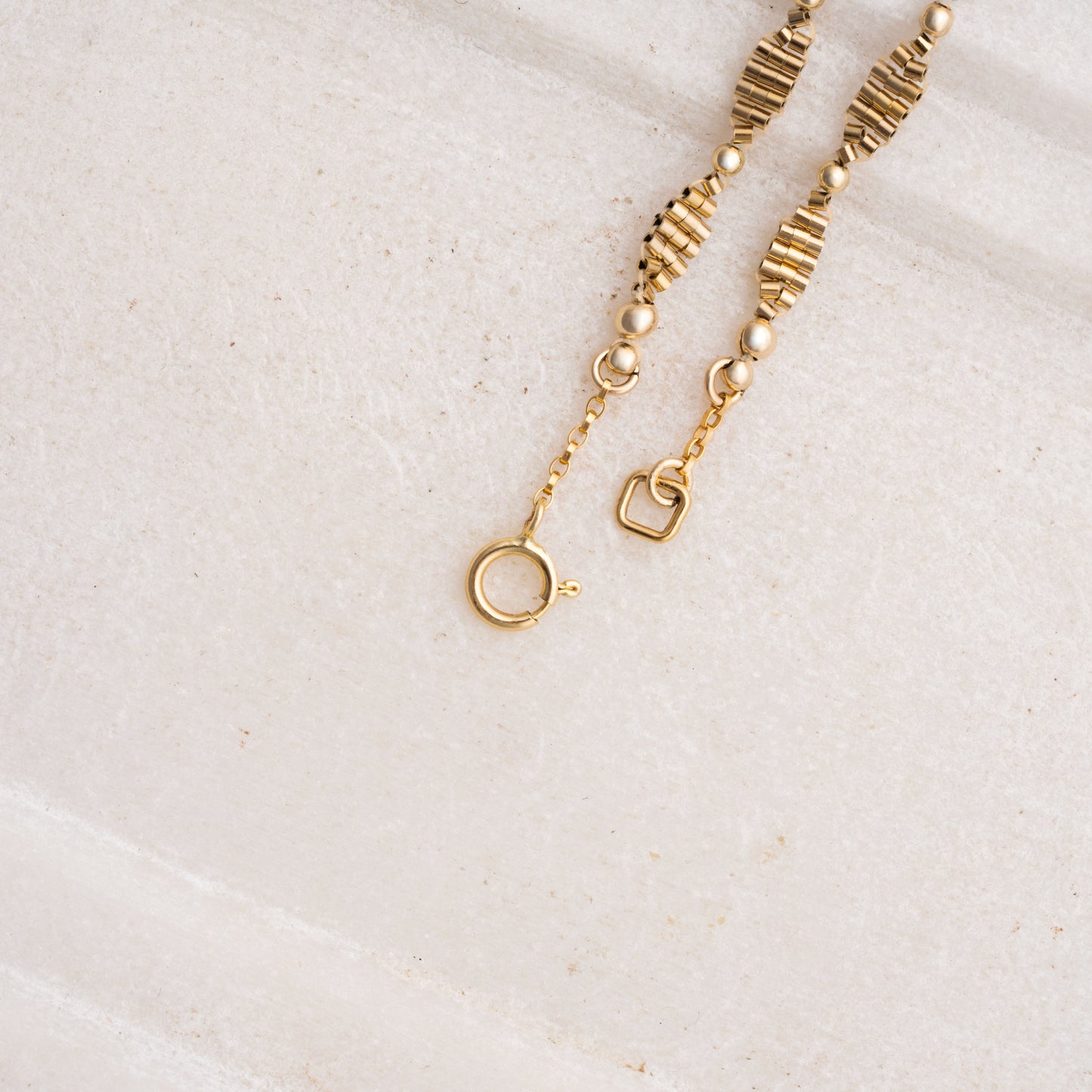 close up view of clasps on a gold-filled beaded necklace laying on a white marble tray