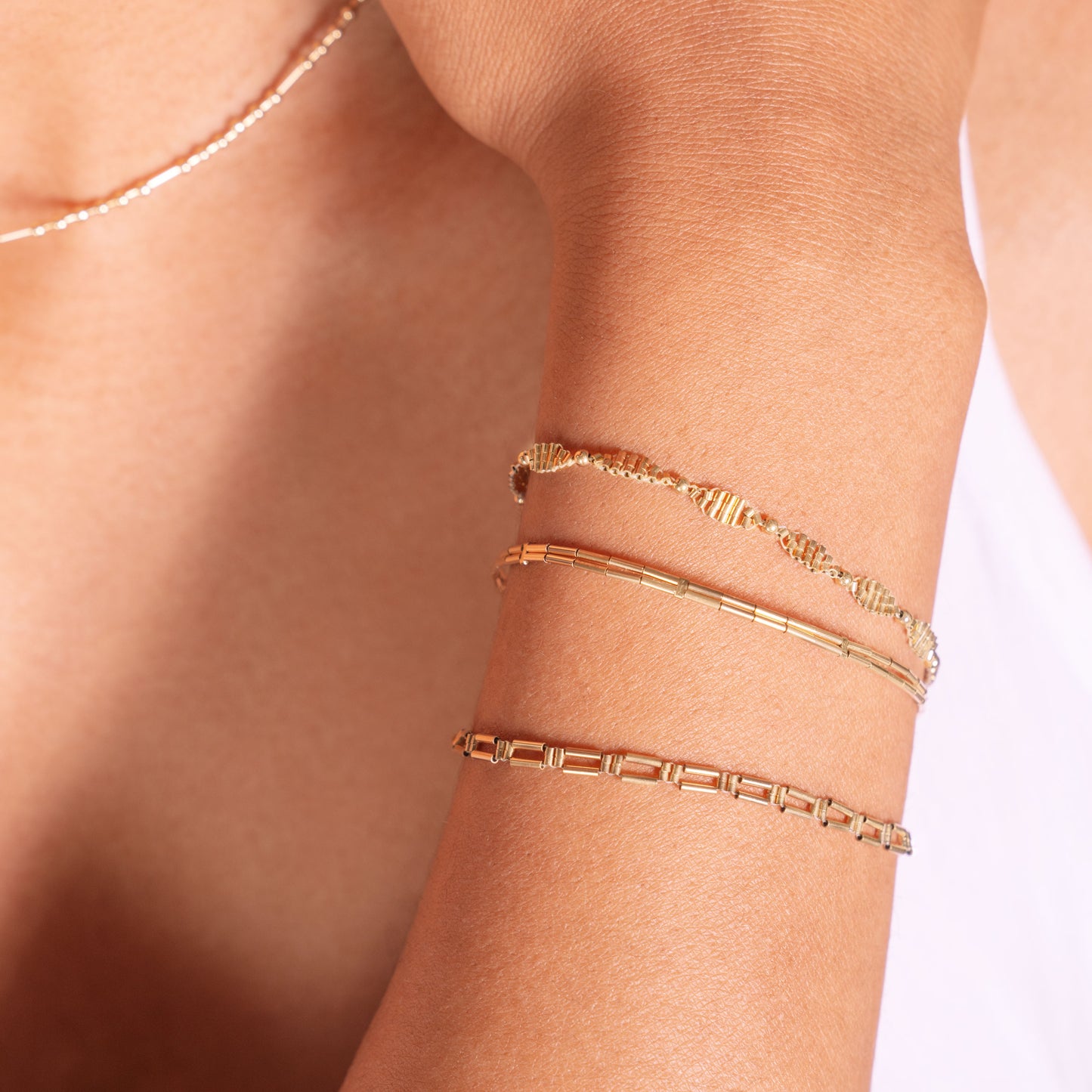 woman showing wrist with 3 gold-filled bracelets and wearing a white-beaded necklace and white top