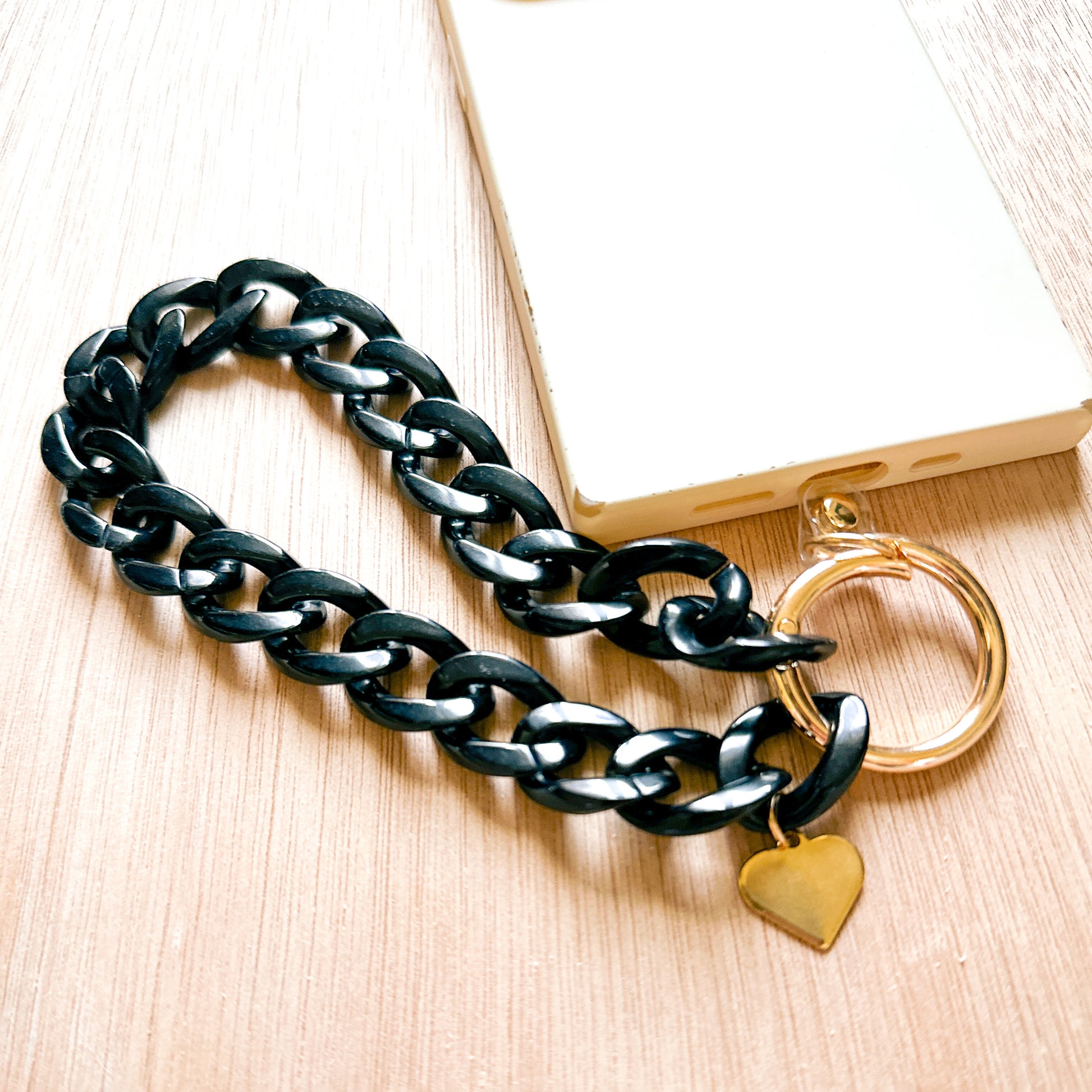 shiny black acrylic links with a heart charm on a gold ring tethered to a phone case
