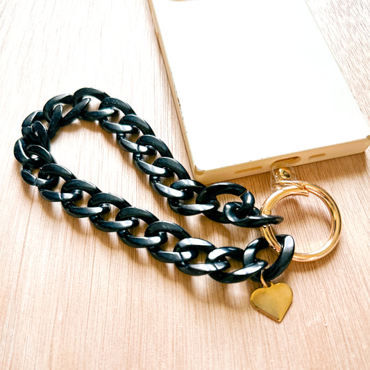 shiny black acrylic links with a heart charm on a gold ring tethered to a phone case