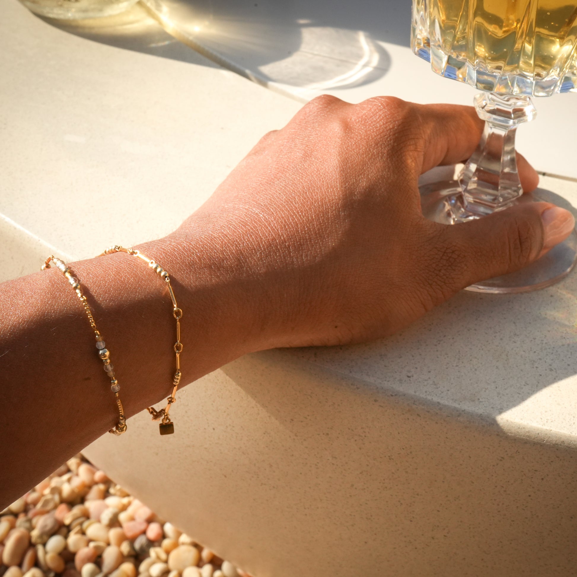 woman's wrist and hand holding a wine glass wearing two bracelets