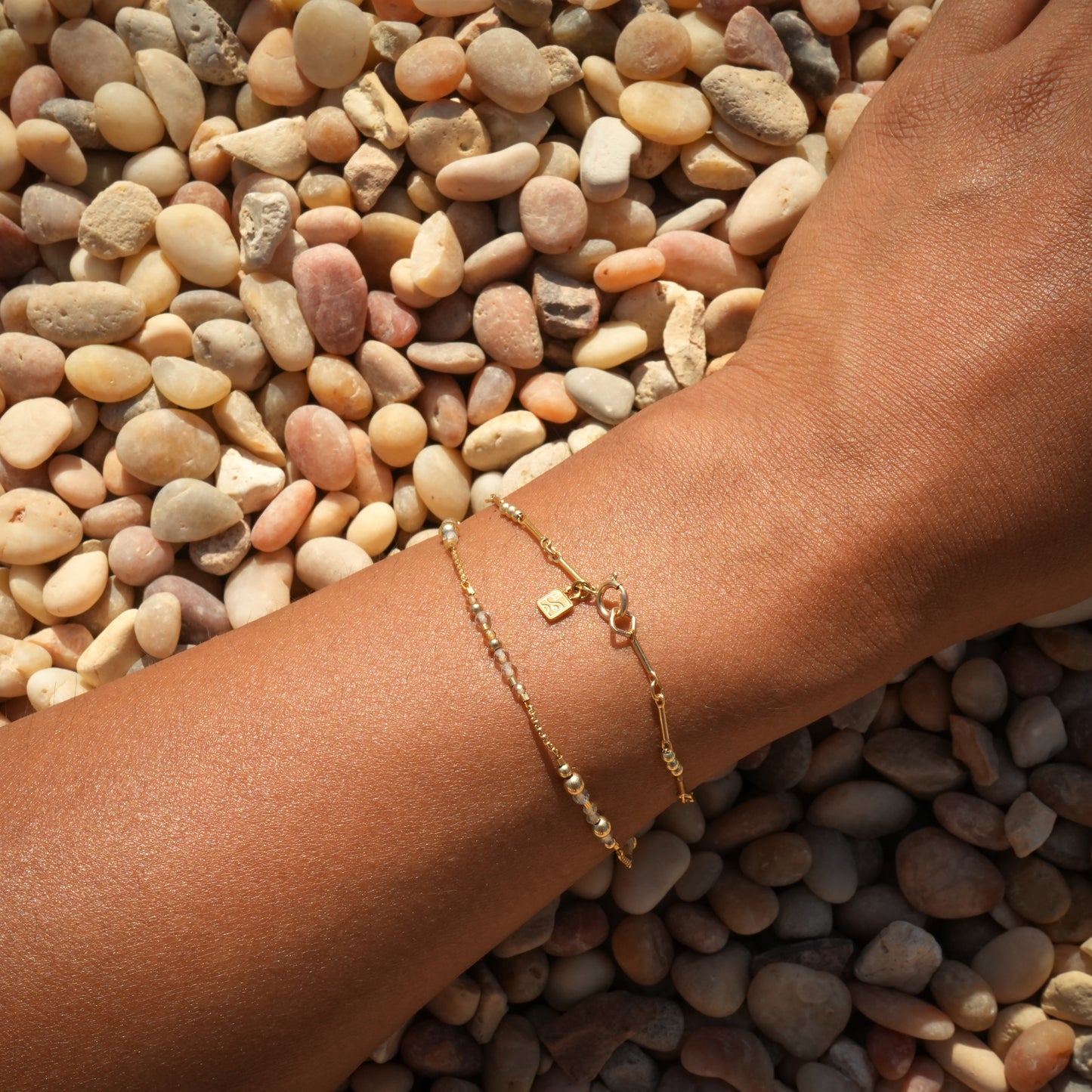 woman's wrist with two bracelets including a gold-fill beaded bracelet with logo charm