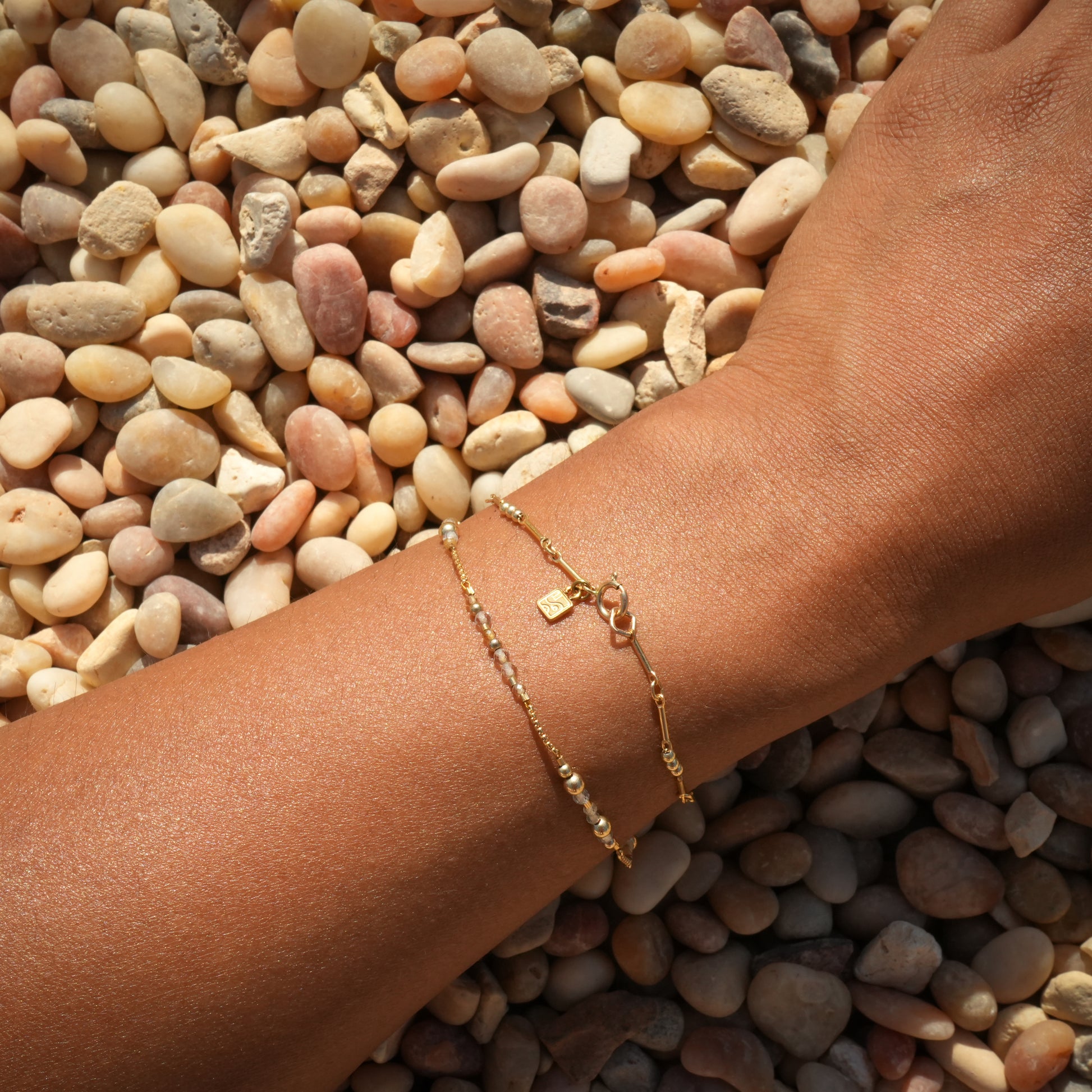 woman's wrist with two bracelets including a gold-fill beaded bracelet with logo charm