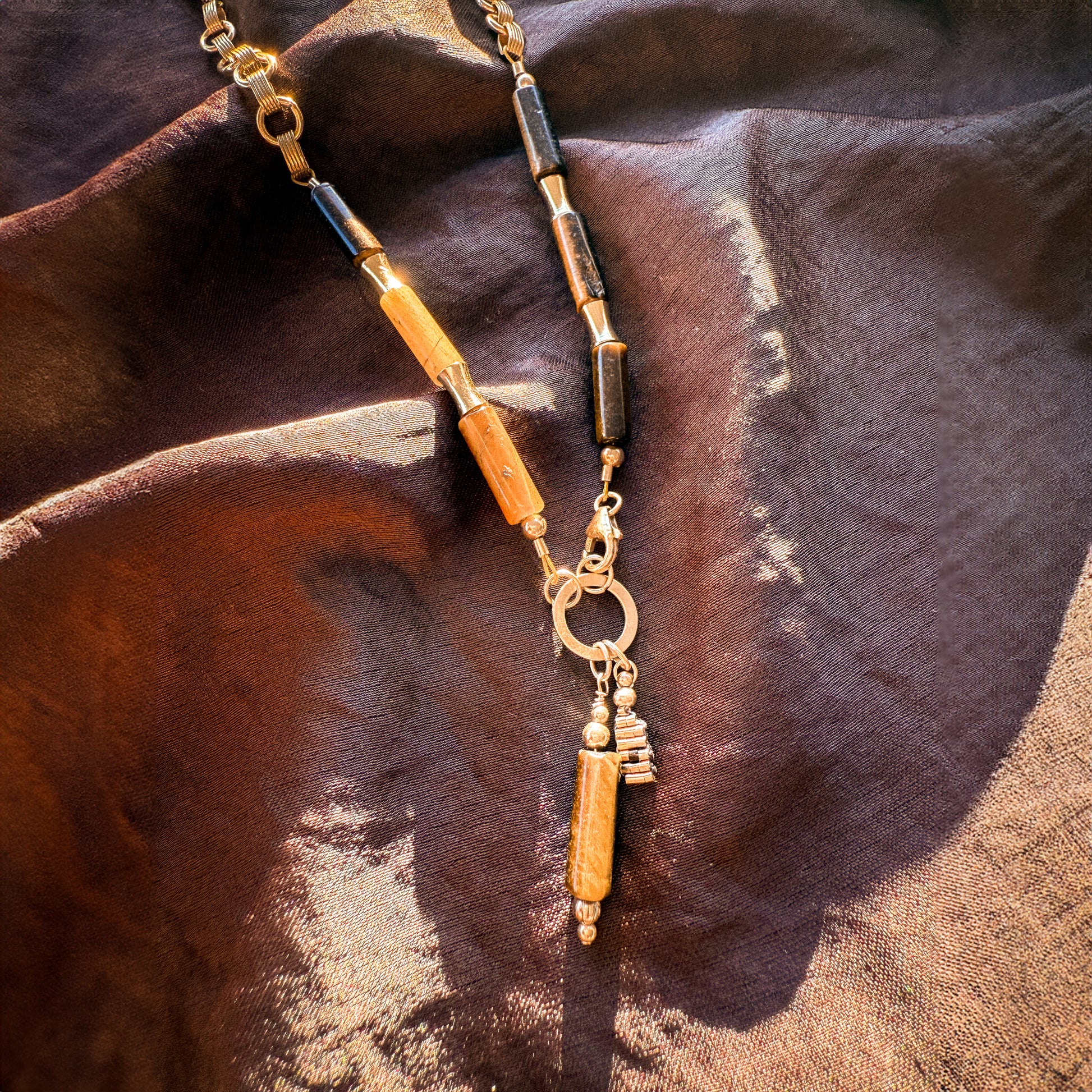 close up view of the front of a necklace with a gold ring and dangling accents including tiger's eye beads and gold-filled beads handcrafted in a stacked shape