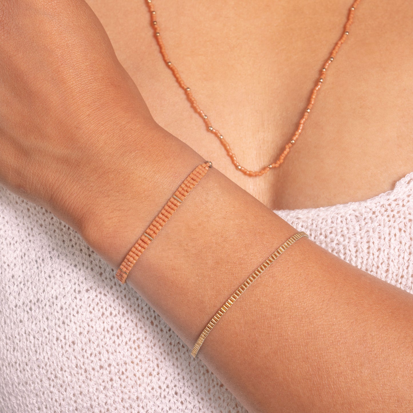 woman showing her wrist and upper chest wearing two bracelets and a necklace with coral-colored glass beads and gold-filled beads