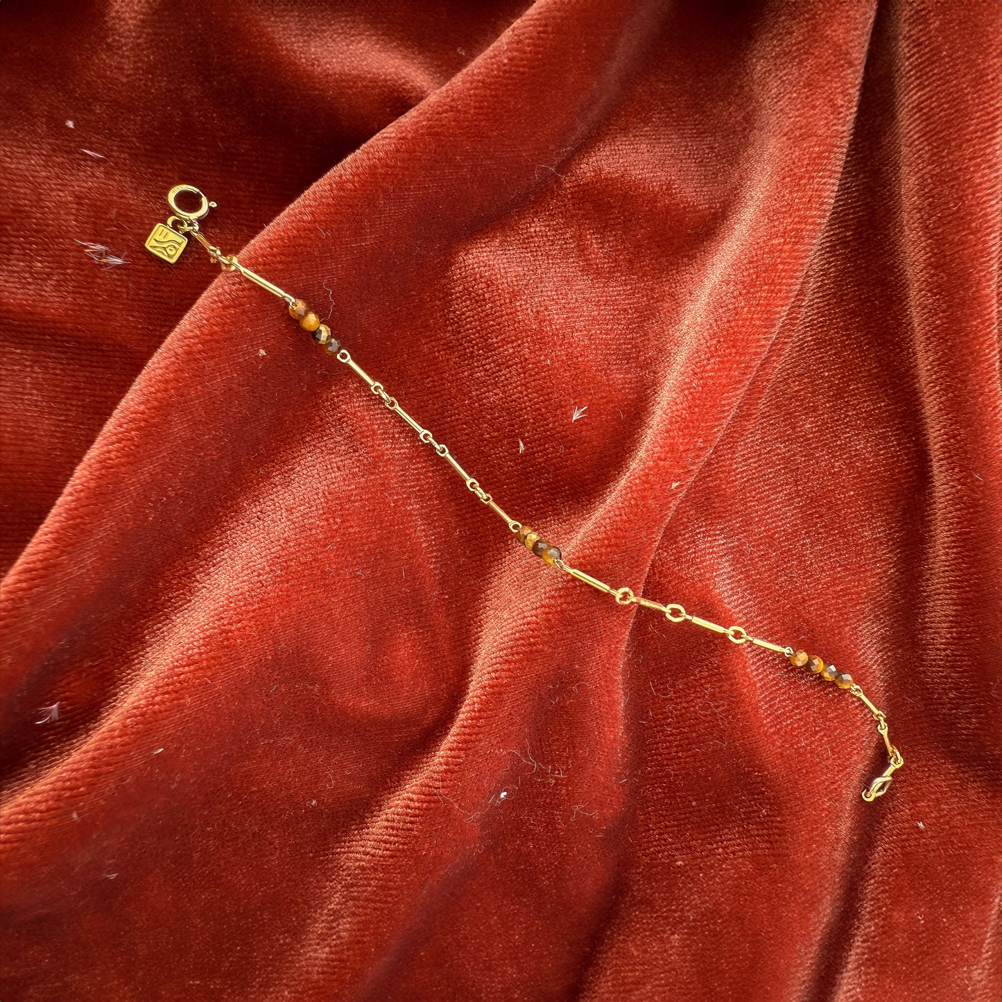 bracelet with tiger's eye and gold-filled beads on a red cloth with a So Niice logo charm