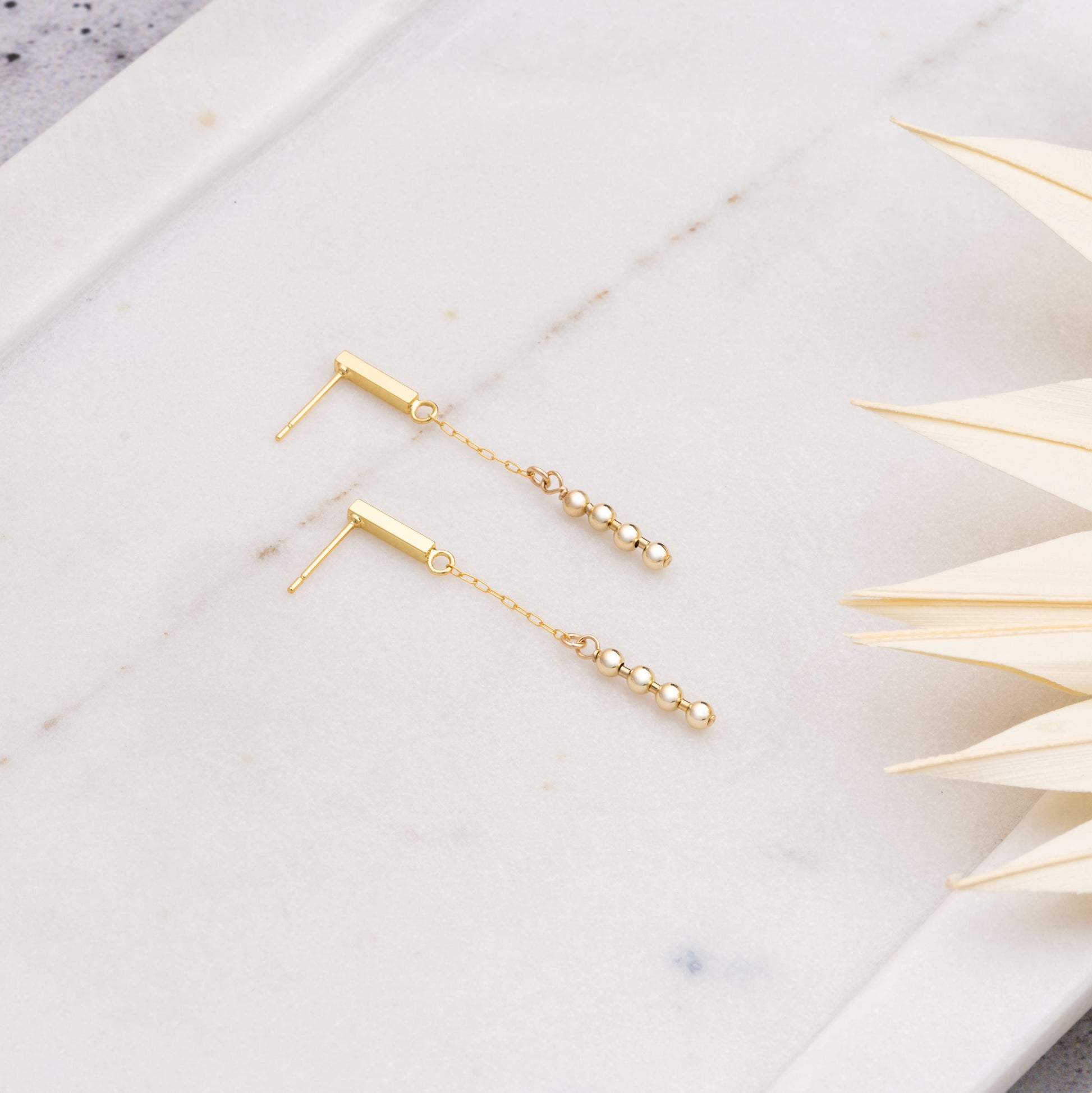 gold-filled dangling beaded earrings on a marble tray