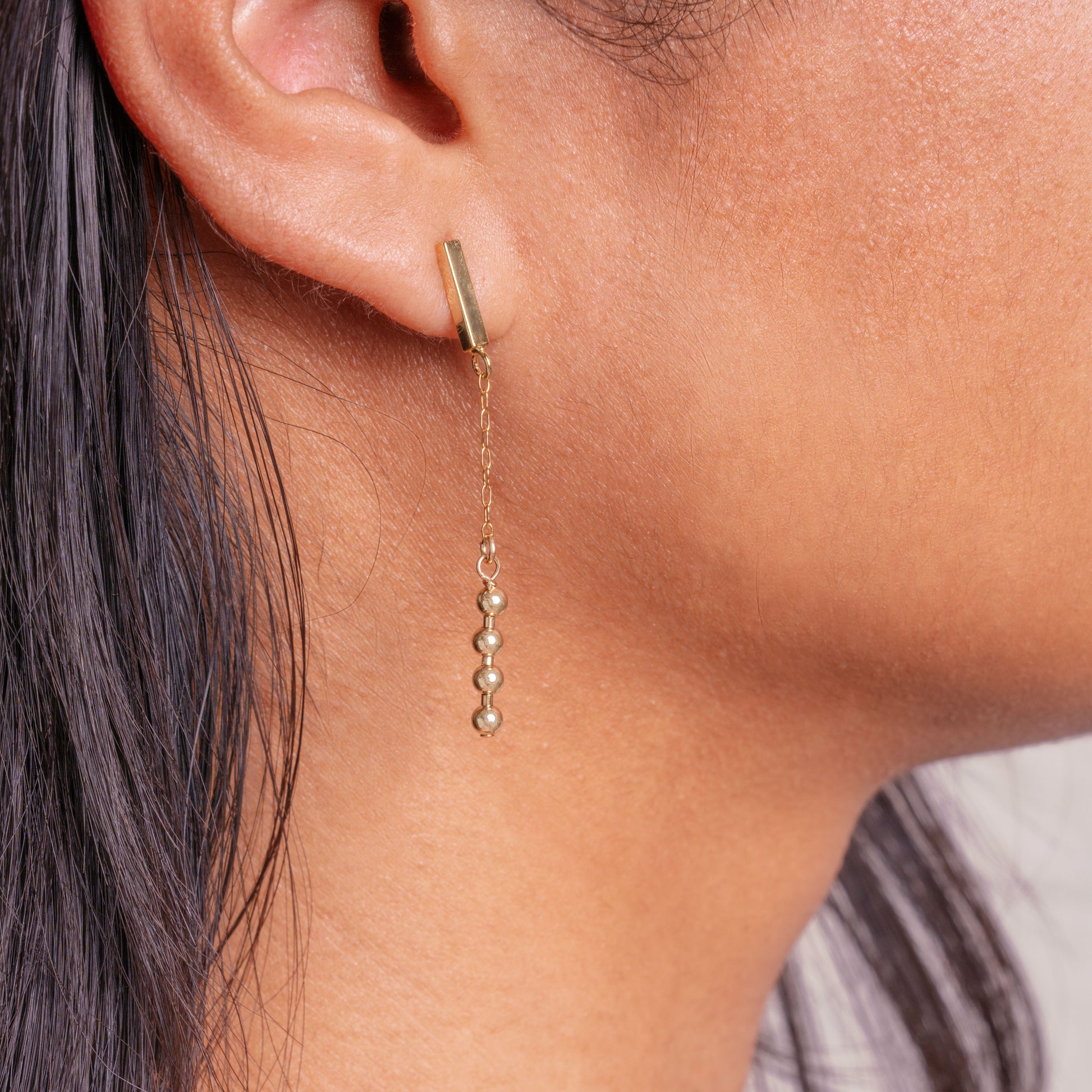 Asian-American woman's right ear wearing a gold-filled beaded dangling earring