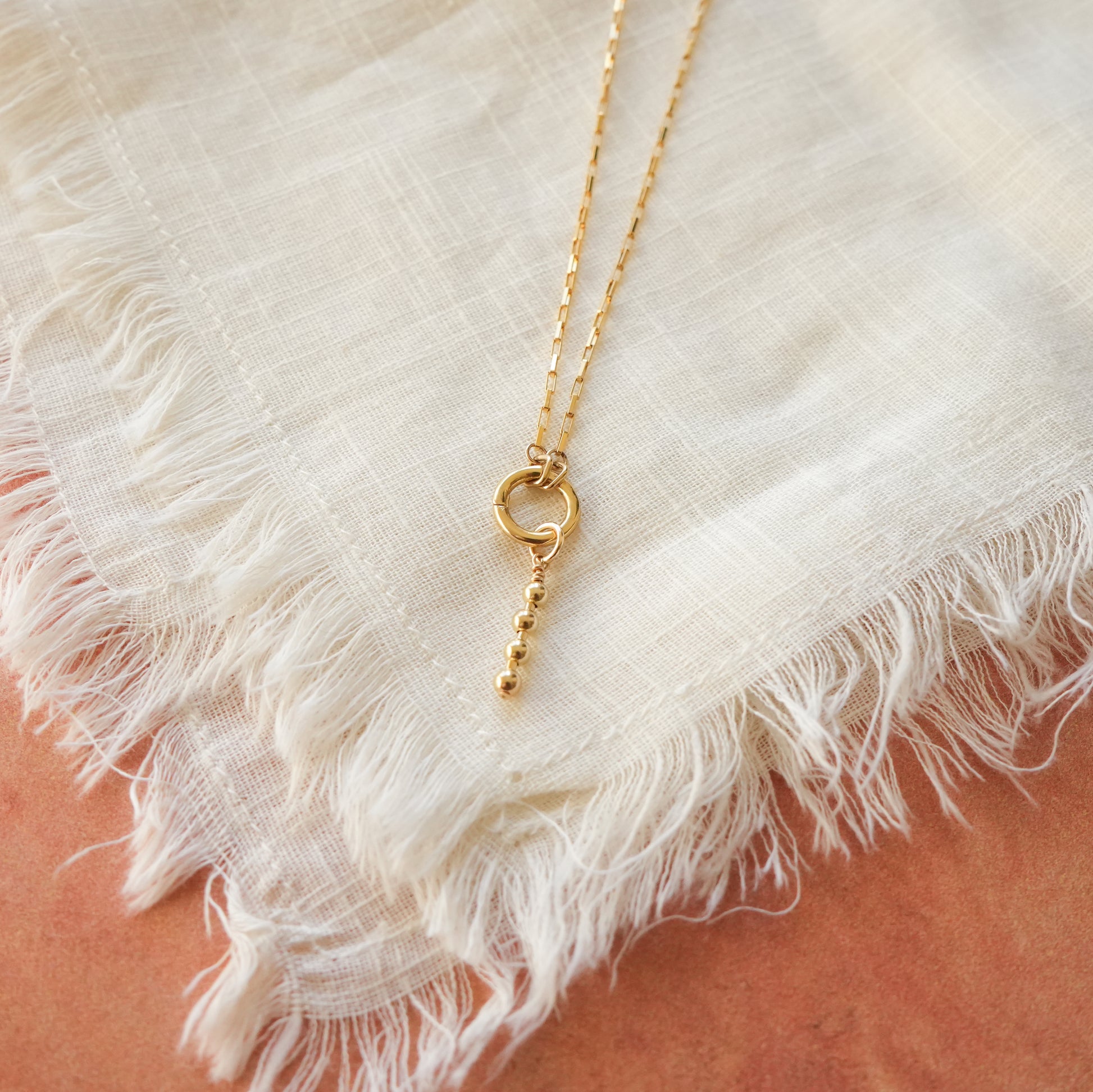 close-up view of gold-filled circle front clasp and dangling accent charm with four gold-filled ball beads
