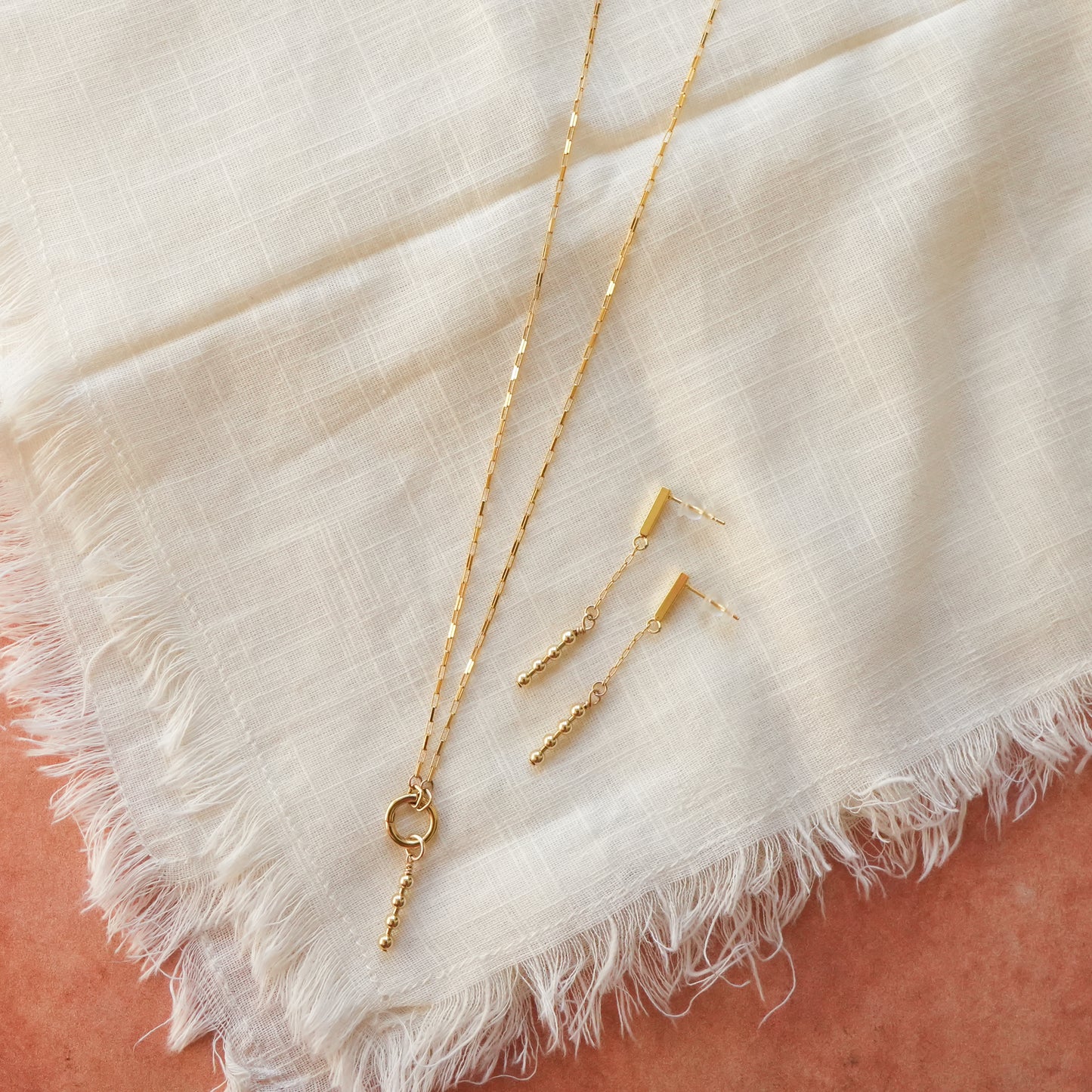 gold-filled chain necklace and a pair of matching gold-filled dangling beaded earrings on a white cloth