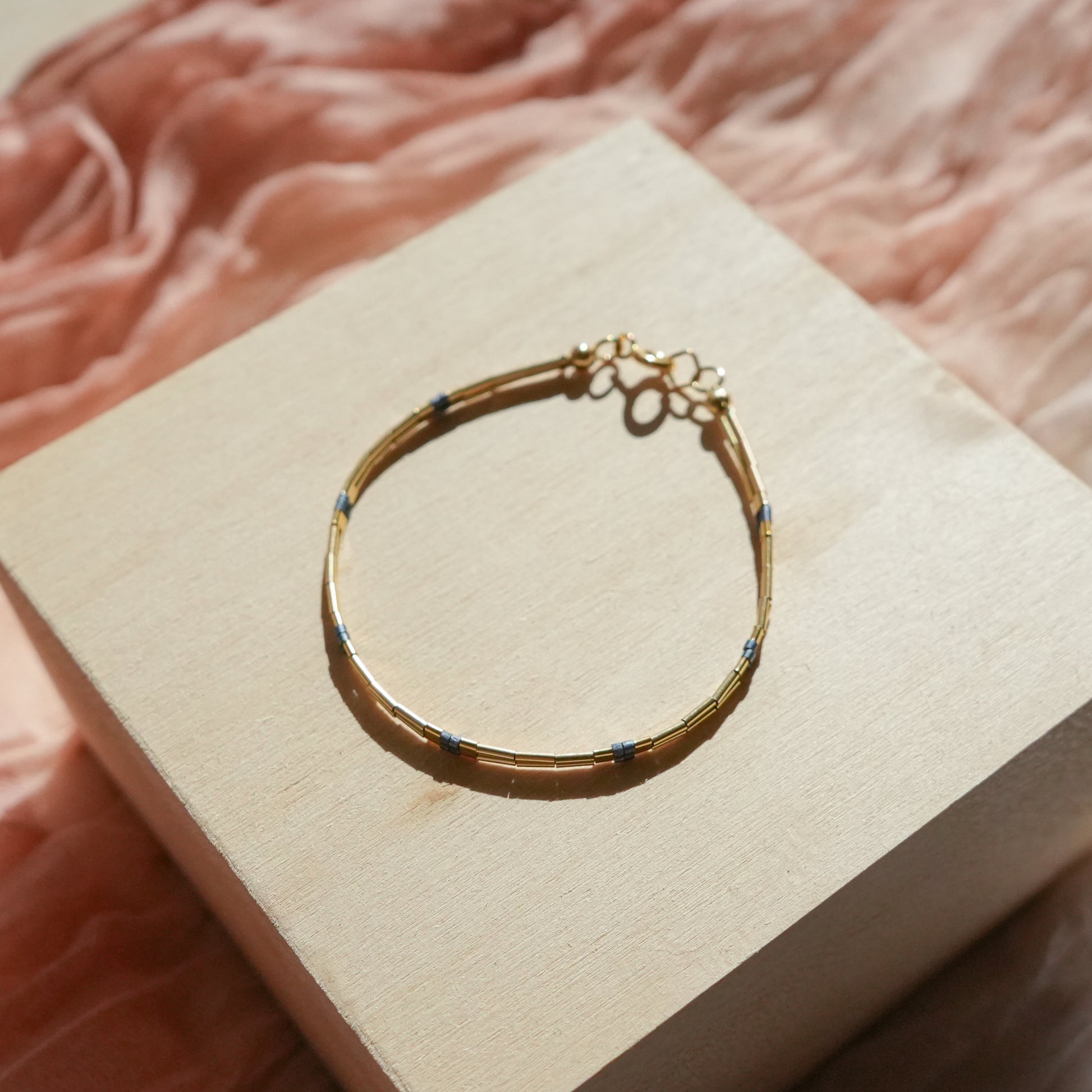 bracelet with 14k gold-fill beads and matte blue-gray glass beads on a wooden block