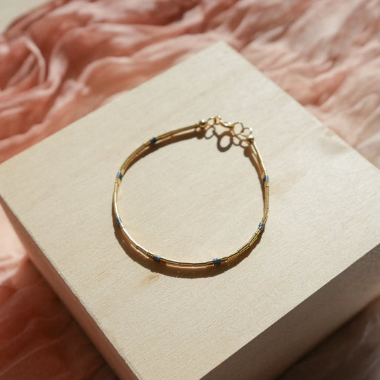 bracelet with 14k gold-fill beads and matte blue-gray glass beads on a wooden block