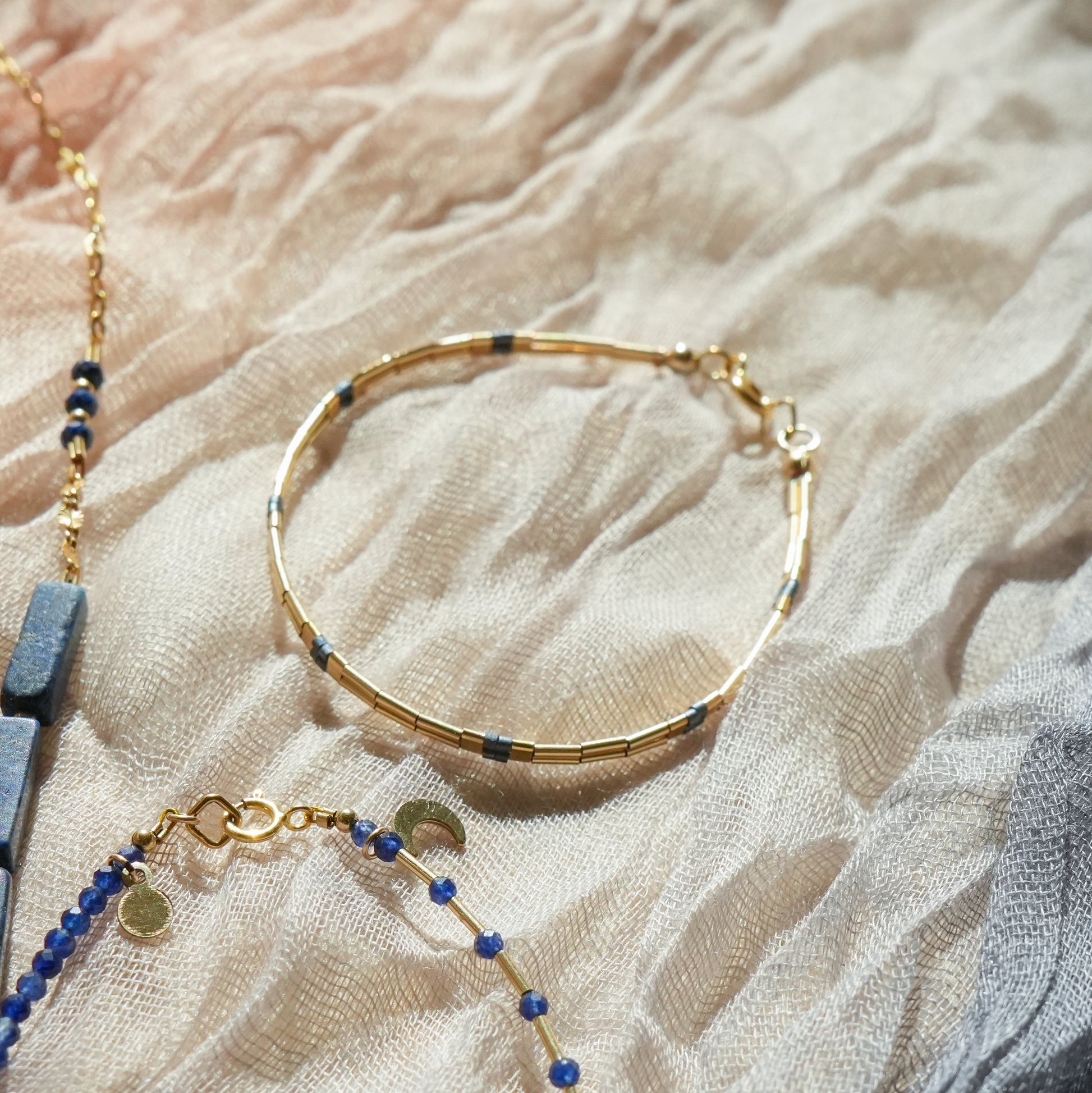 14k gold-fill and blue-grey glass bead bracelet next to a matching bracelet with moon charm and a matching necklace