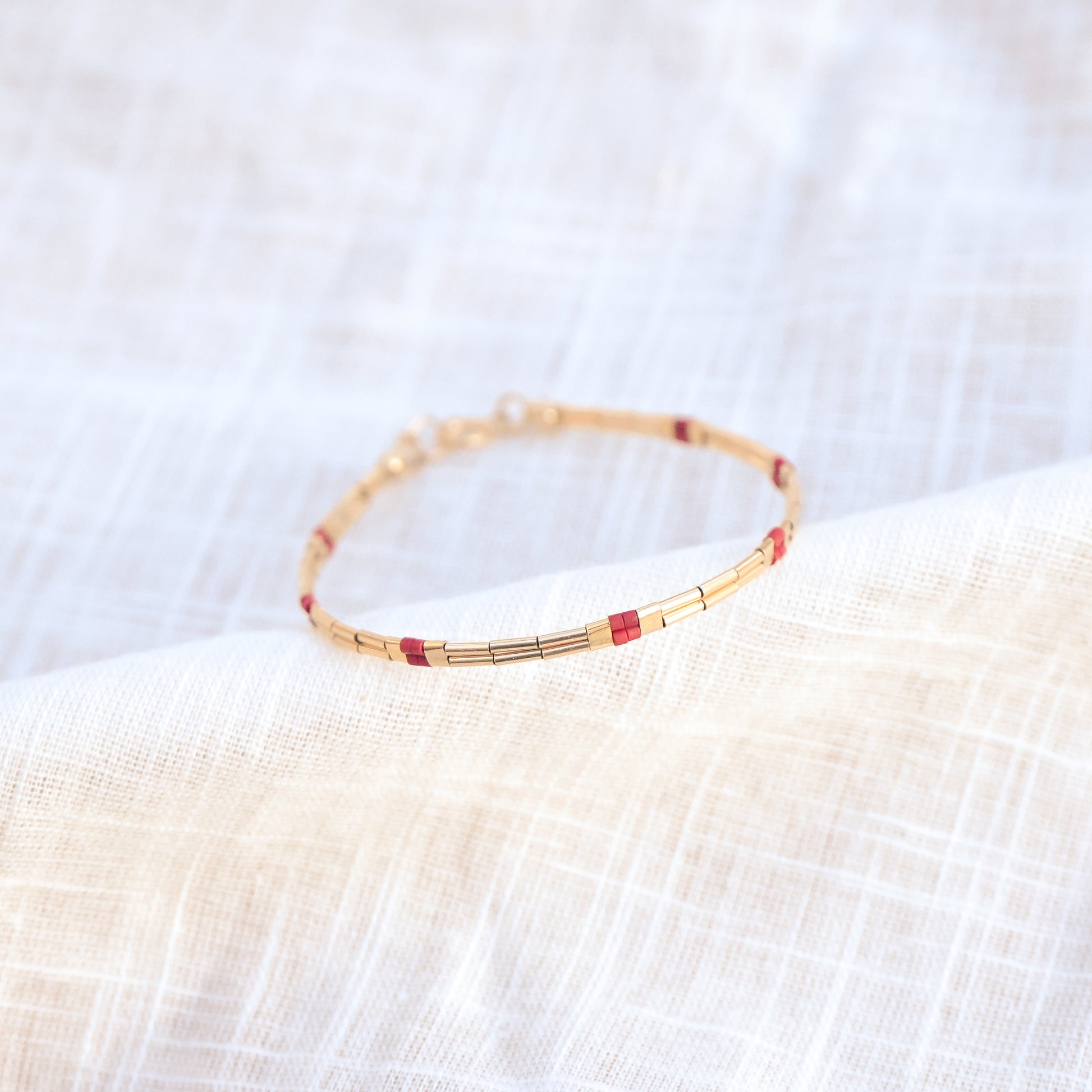 close up view of bracelet with gold-fill and red glass beads on a white cloth