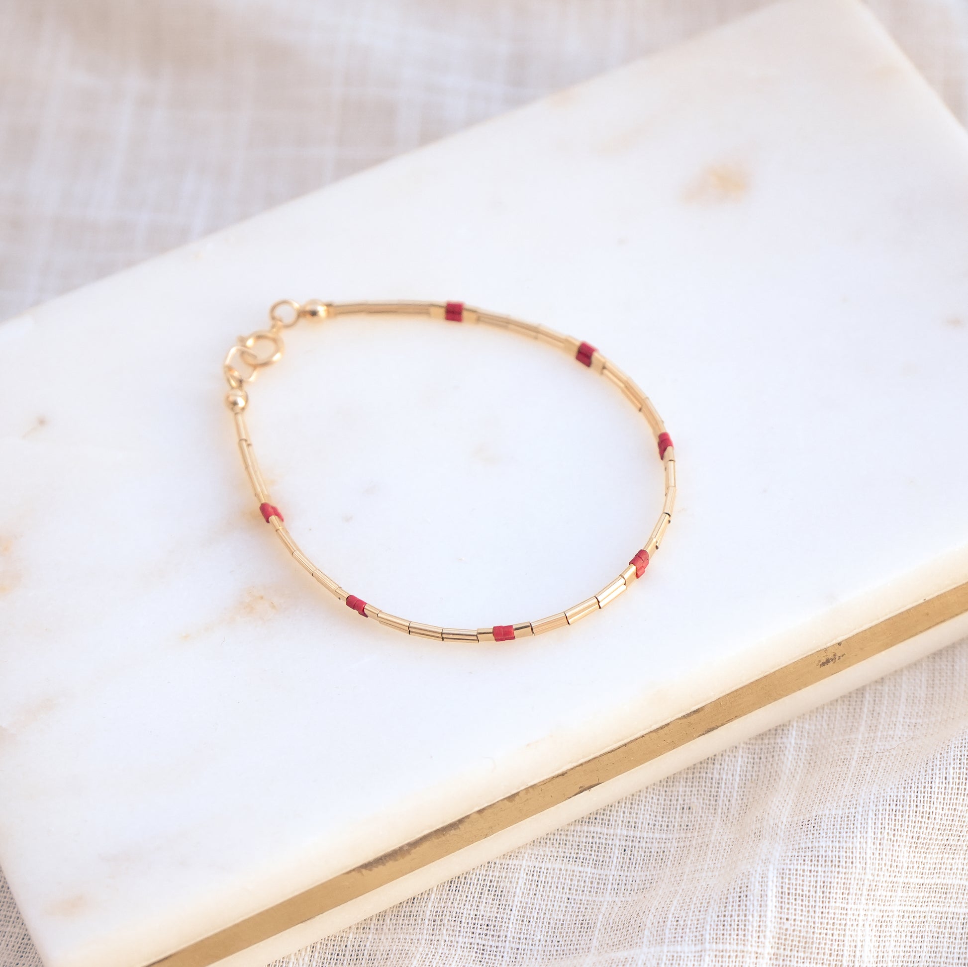 bracelet with gold fill and red glass beads on a marble surface