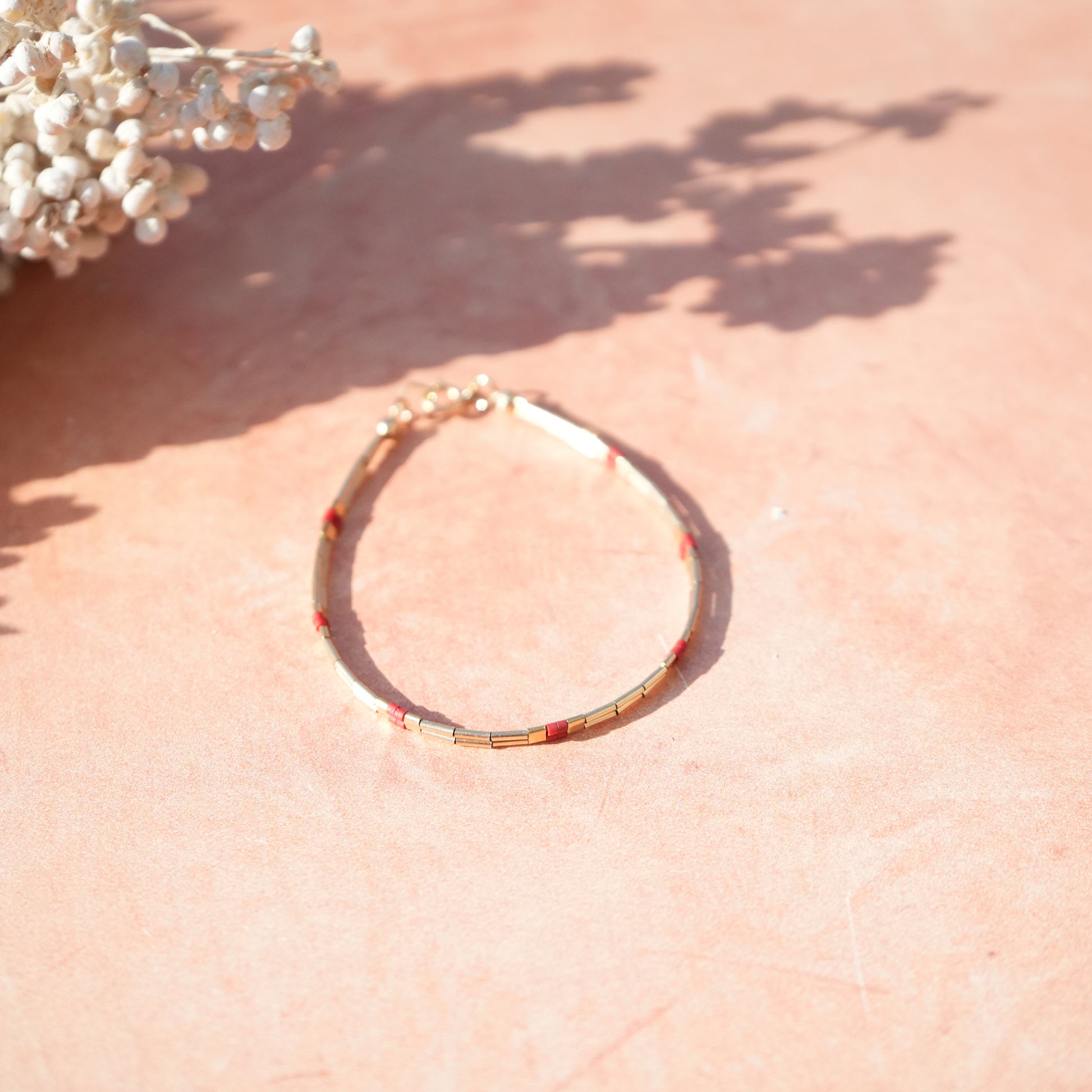 bracelet with 14k gold-fill and red glass beads laying on a red clay surface in the sun