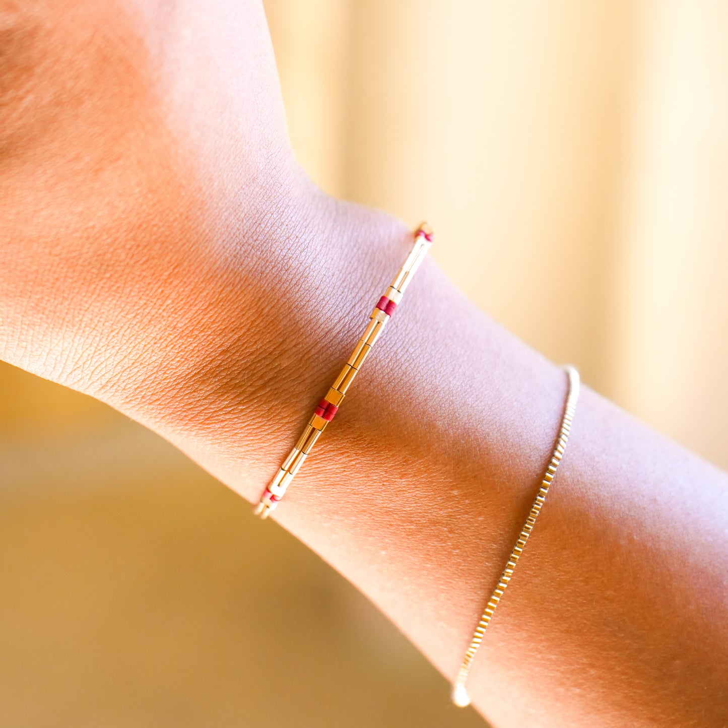 woman's wrist wearing a gold-fill bracelet with red glass beads and a dainty gold-fill bracelet