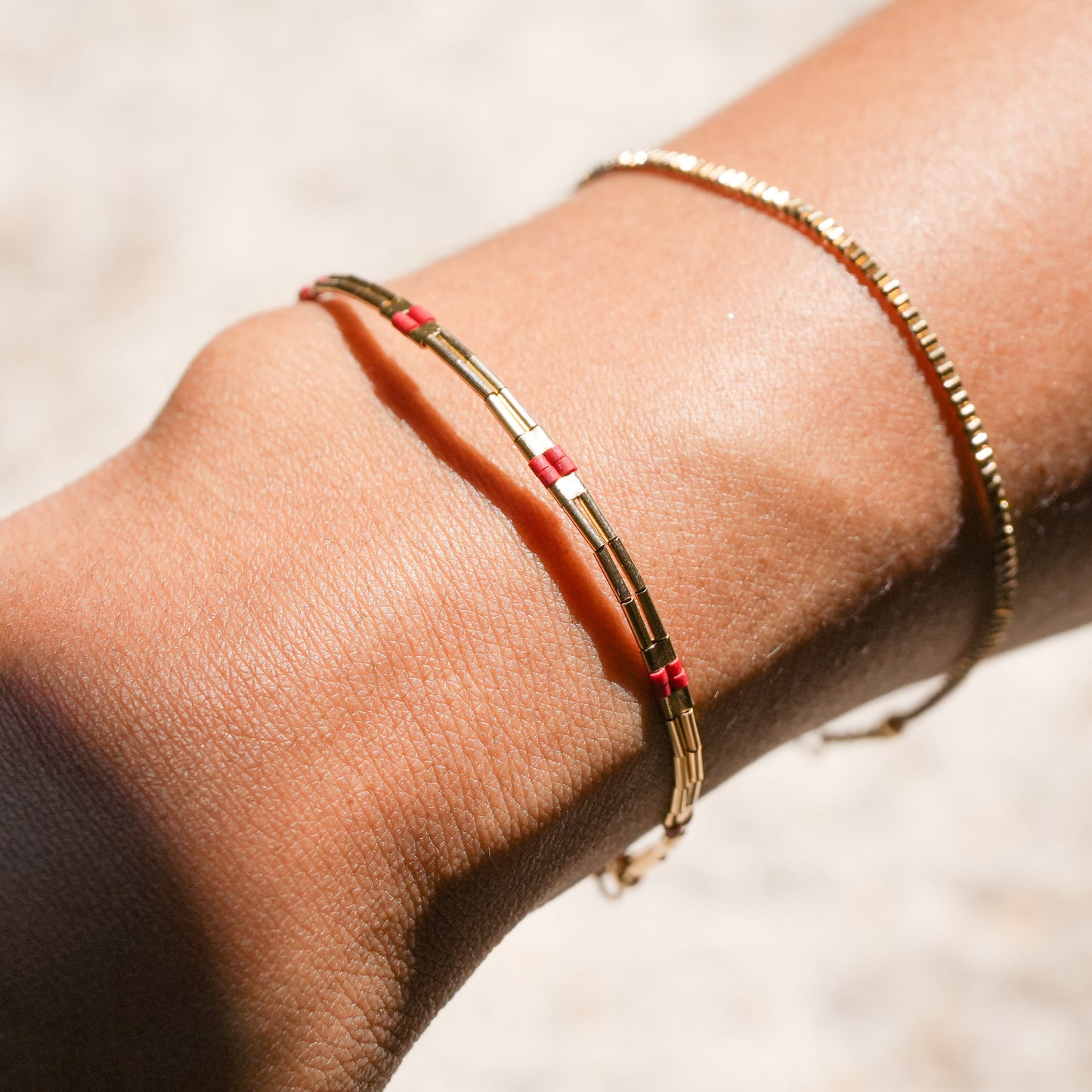 close up view of a woman's wrist wearing a bracelet with gold-fill and red glass beads and a dainty gold bracelet