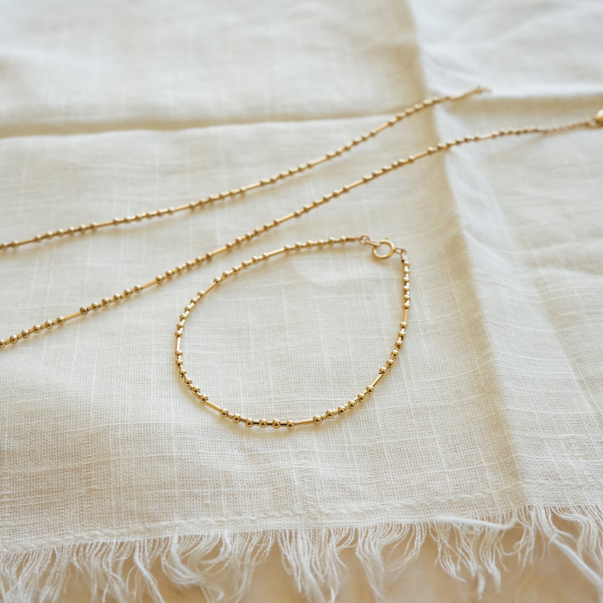 angled view of a gold fill bead bracelet with ball and tube beads and matching necklace on a white cloth
