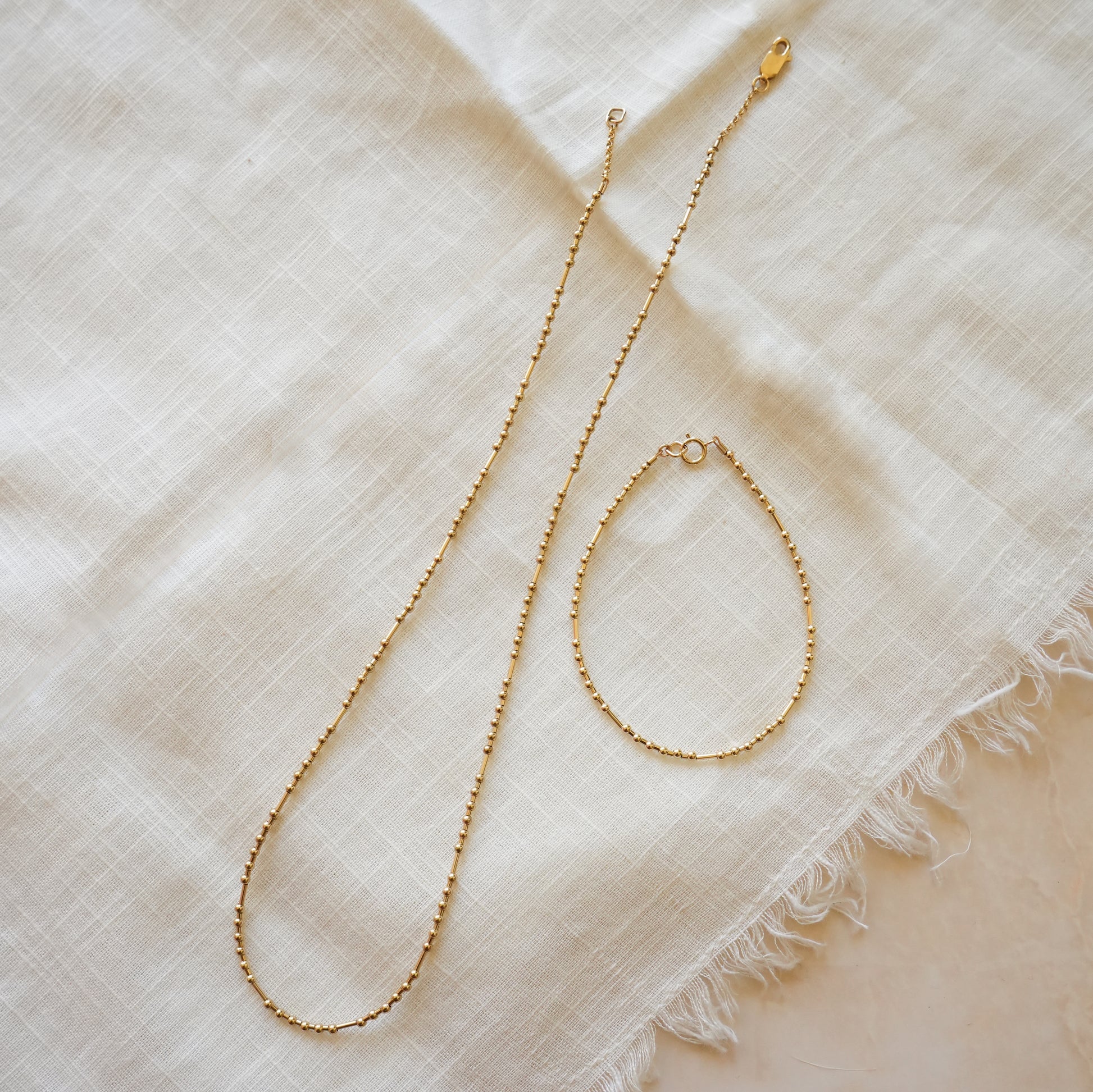 gold fill bead bracelet with ball and tube beads next to a matching gold-fill beaded necklace on a white cloth