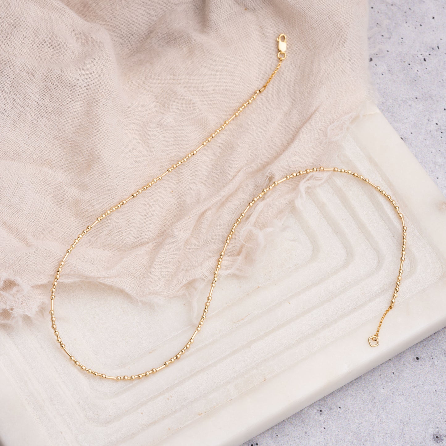 gold fill beaded necklace on a piece of cloth and geometric surface