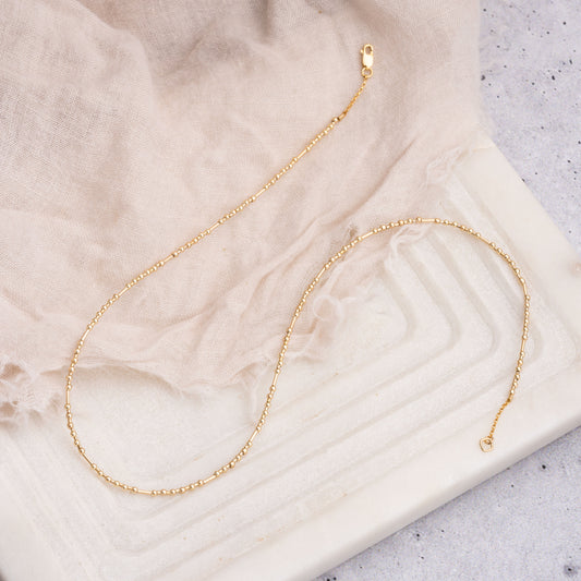 gold fill beaded necklace on a piece of cloth and geometric surface