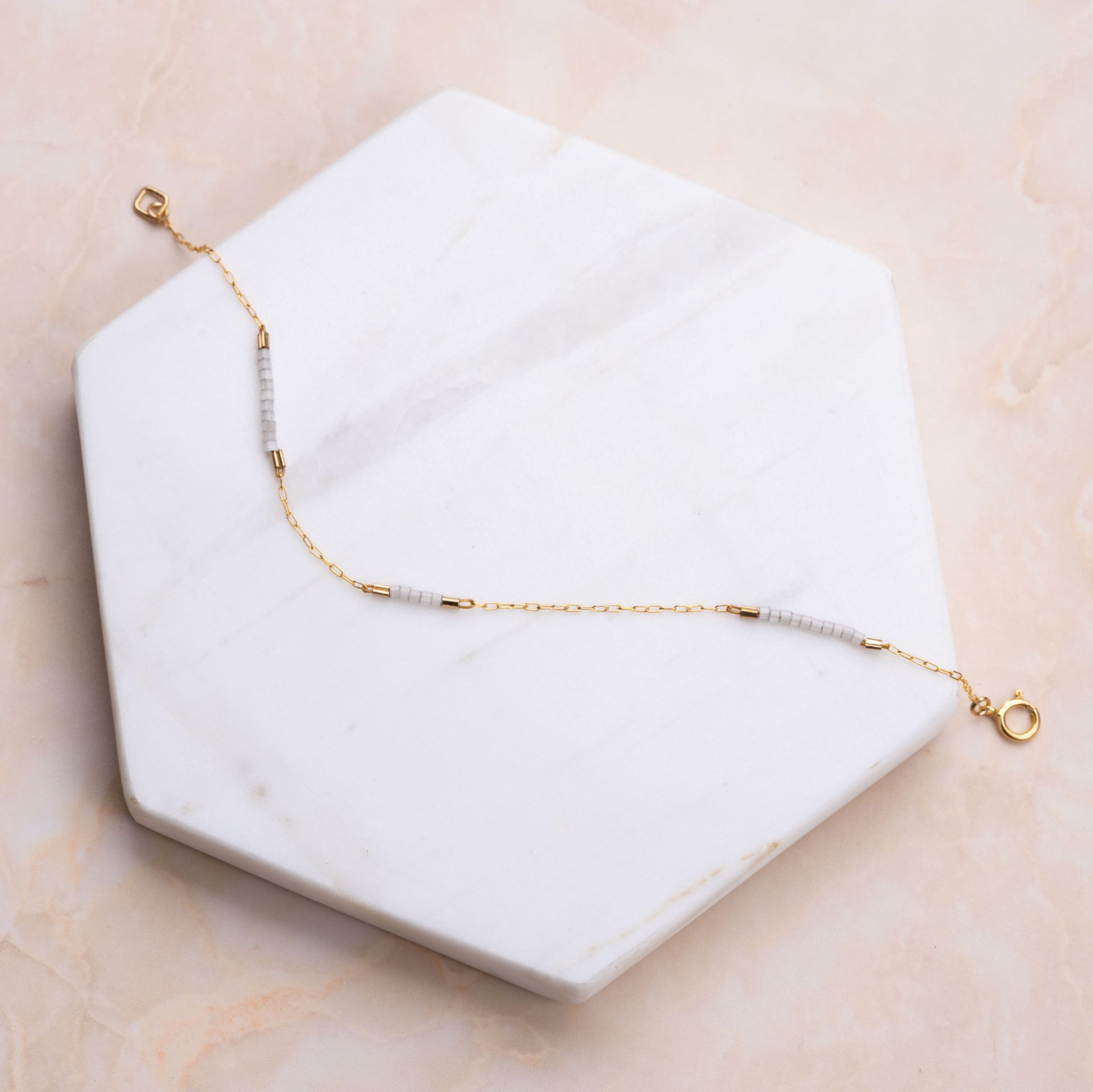 14k gold-fill chain bracelet with white beads on a white marble hexagon-shaped slab