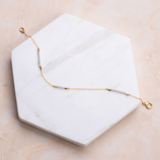 14k gold-fill chain bracelet with white beads on a white marble hexagon-shaped slab