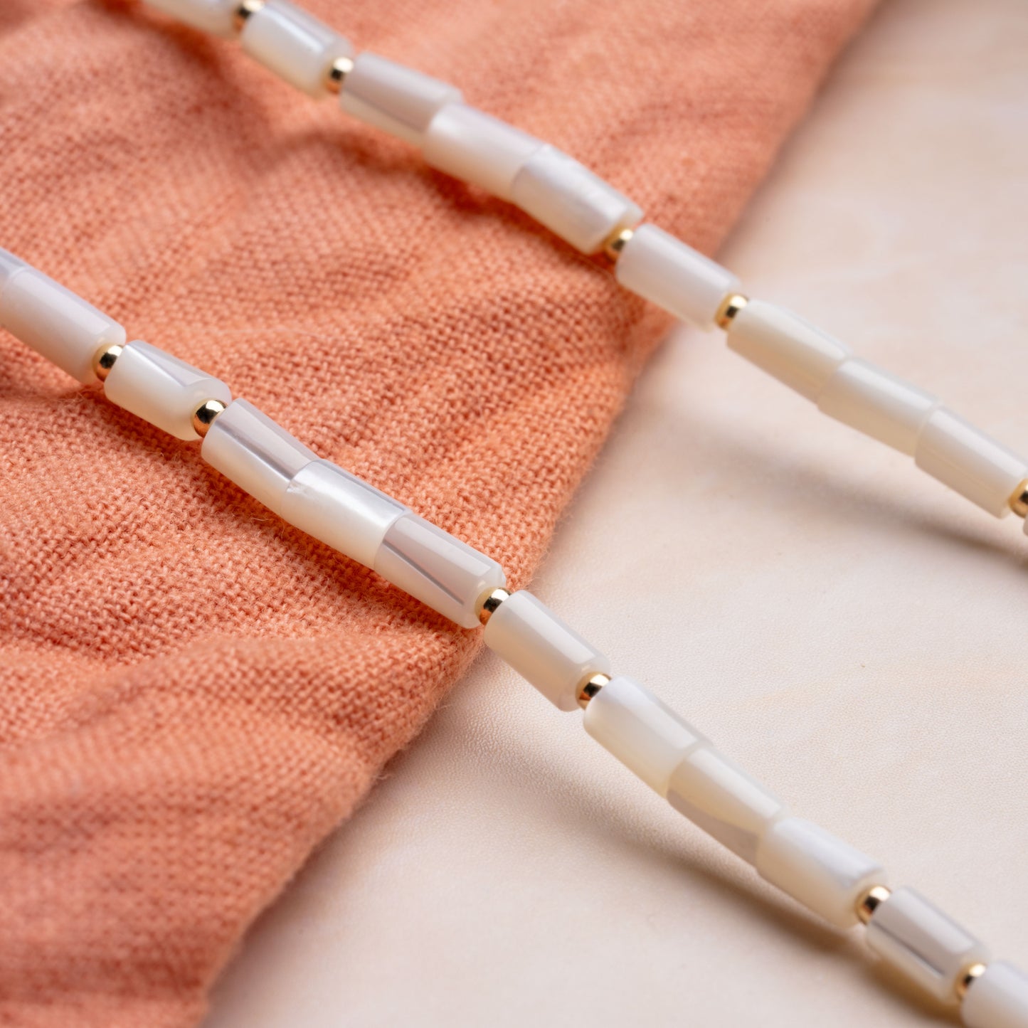 close-up view of mother of pearl tube beads on a necklace resting on a coral cloth