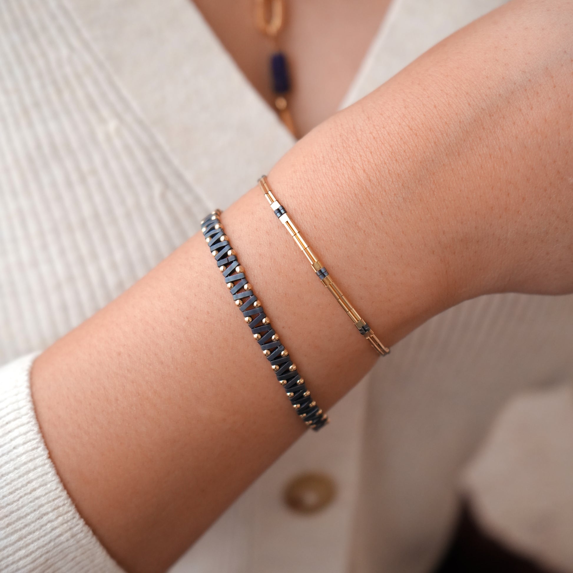 woman's wrist wearing a 14k gold-fill and blue-grey glass bead bracelet as well as a matching blue bracelet with zigzag pattern