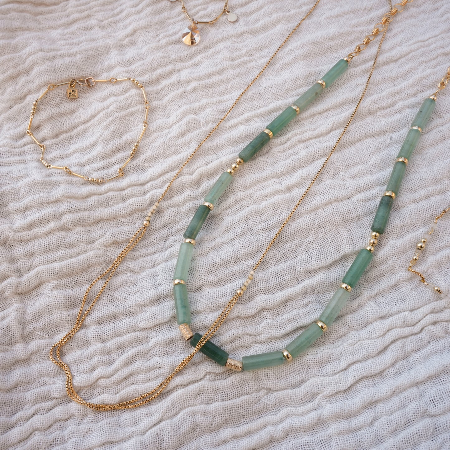 bundle of jewelry on a white cloth including necklaces and bracelets with gold-filled beads and chains