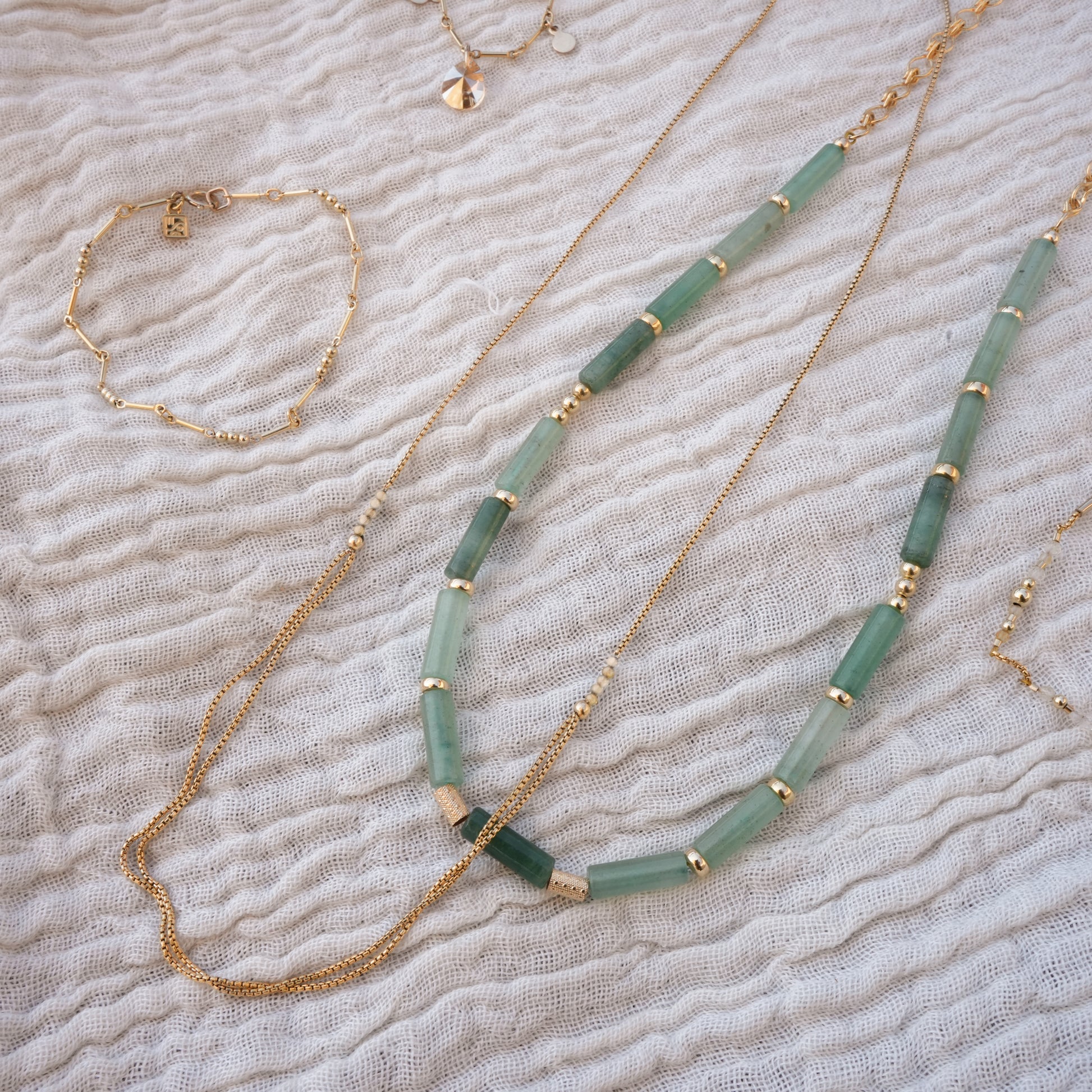bundle of jewelry on a white cloth including necklaces and bracelets with gold-filled beads and chains