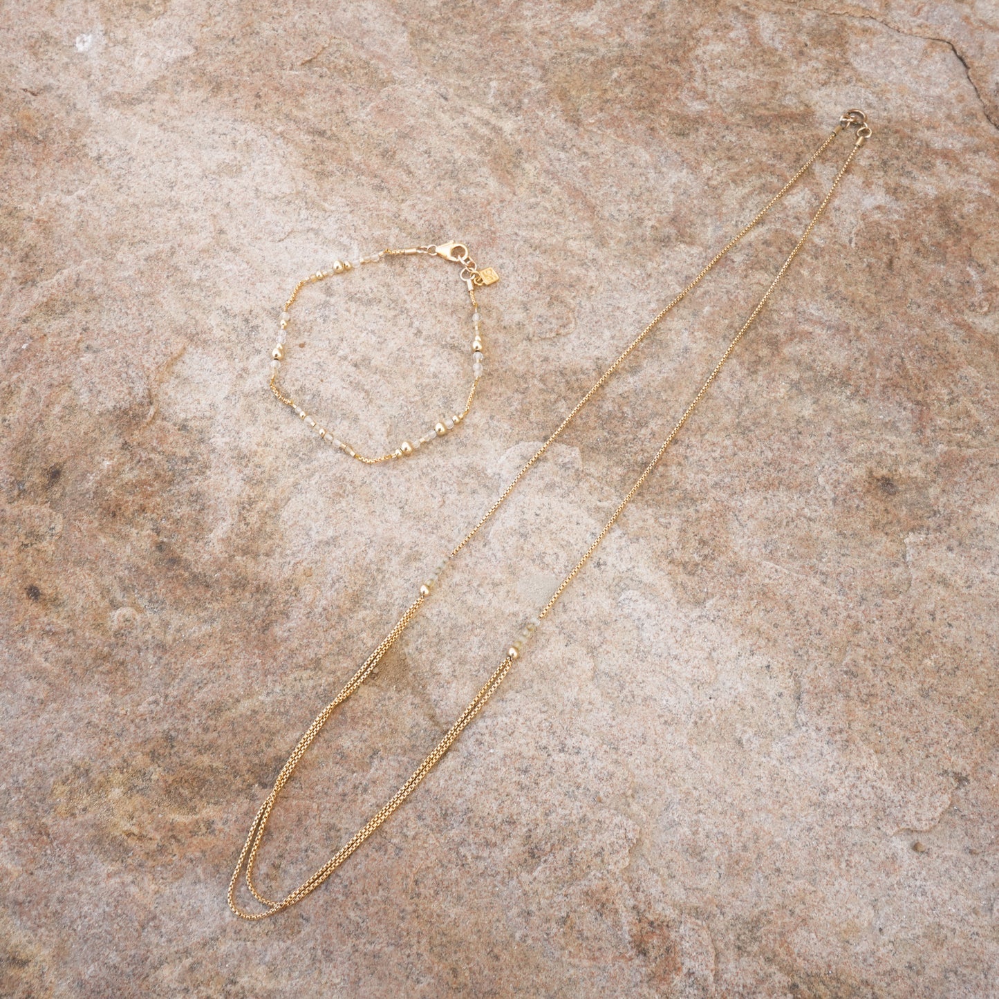 necklace with gold-fill chain and citrine faceted stones next to a beaded bracelet on a stone surface