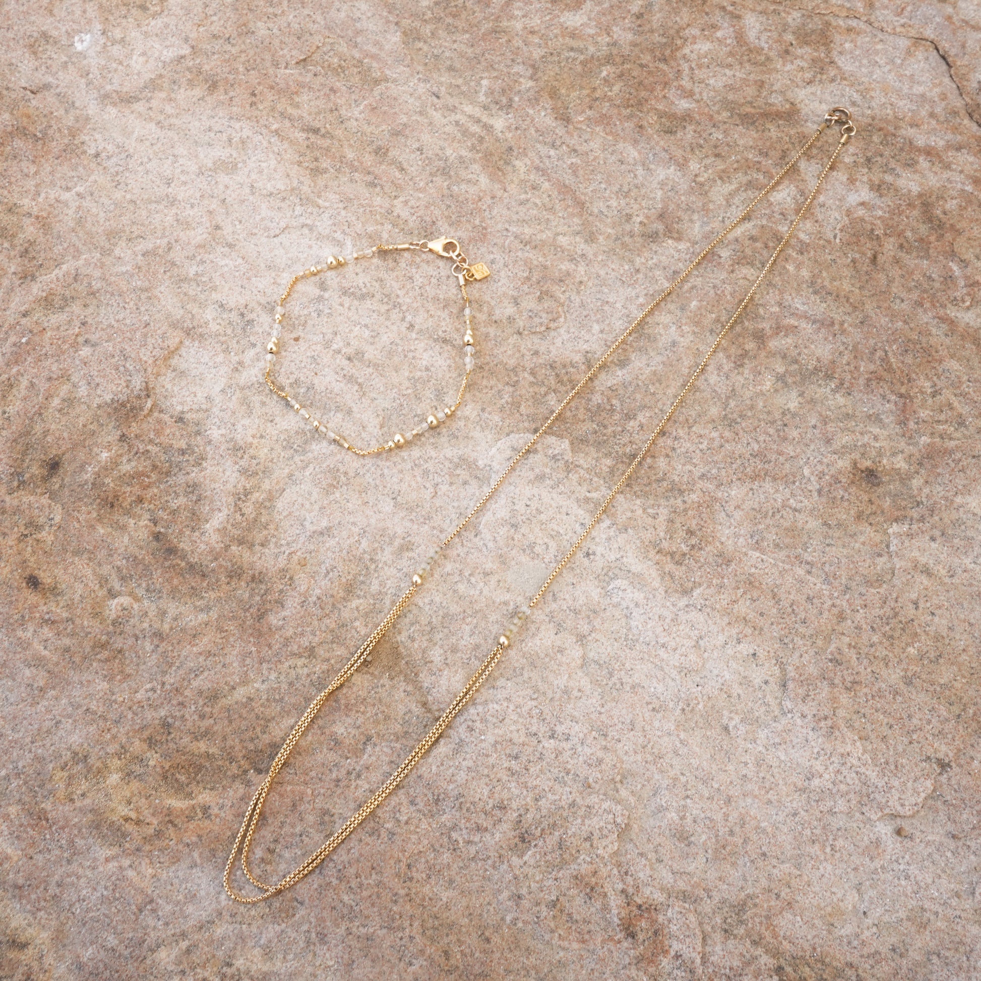 necklace with gold-fill chain and citrine faceted stones next to a beaded bracelet on a stone surface