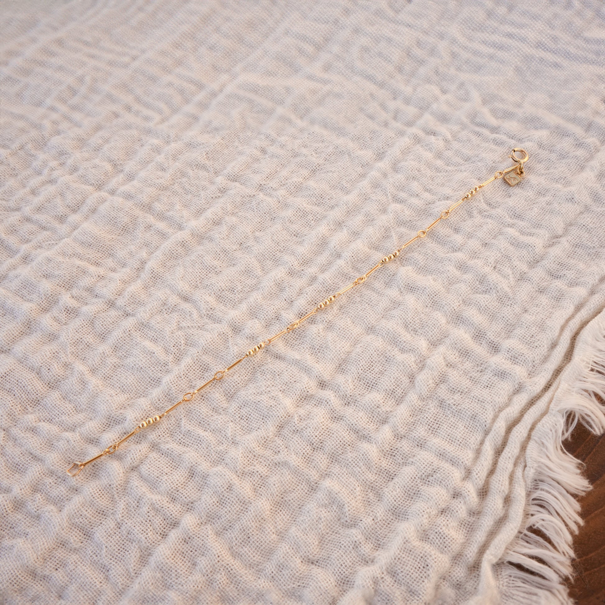 gold-fill beaded bracelet with logo charm on a white cloth
