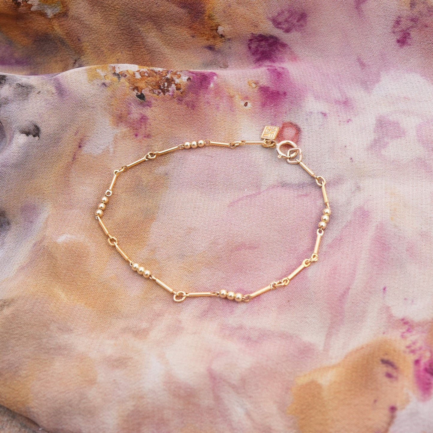 gold-fill beaded bracelet with logo charm on a colorful scarf