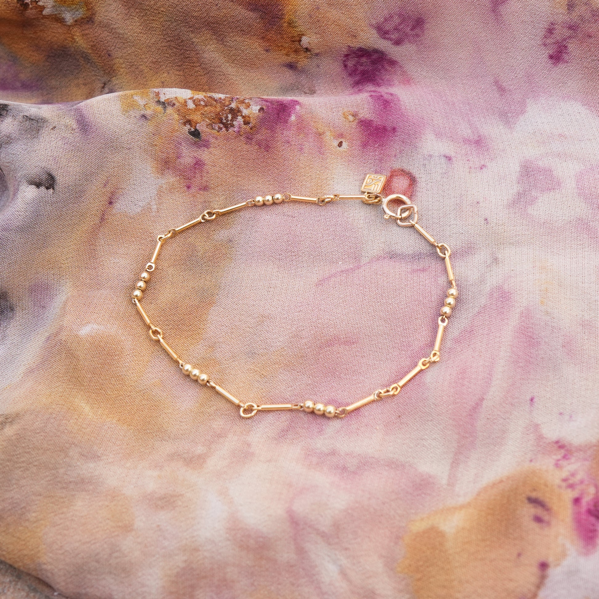 gold-fill beaded bracelet with logo charm on a colorful scarf