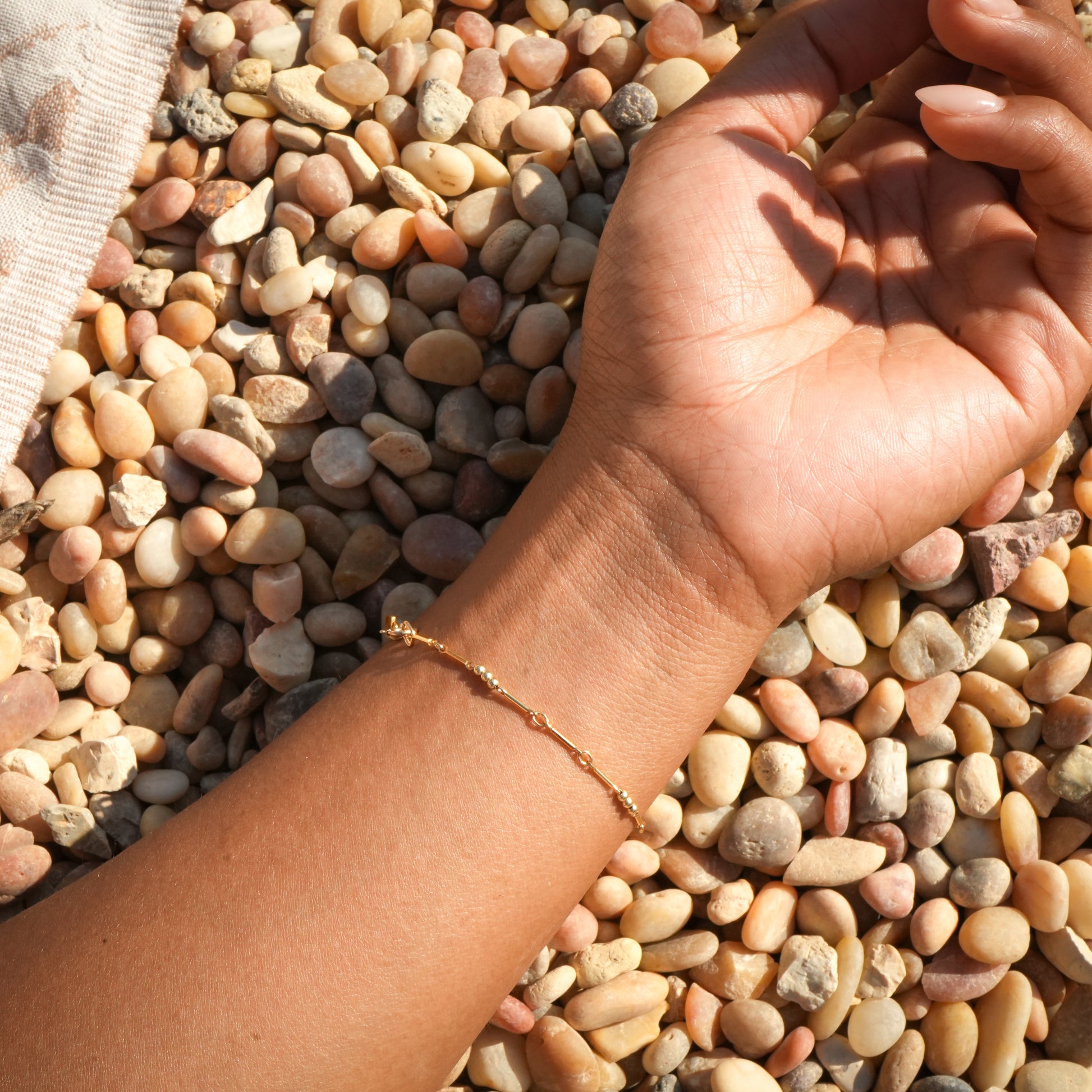 woman's wrist with gold-fill beaded bracelet resting on a bed of pebbles