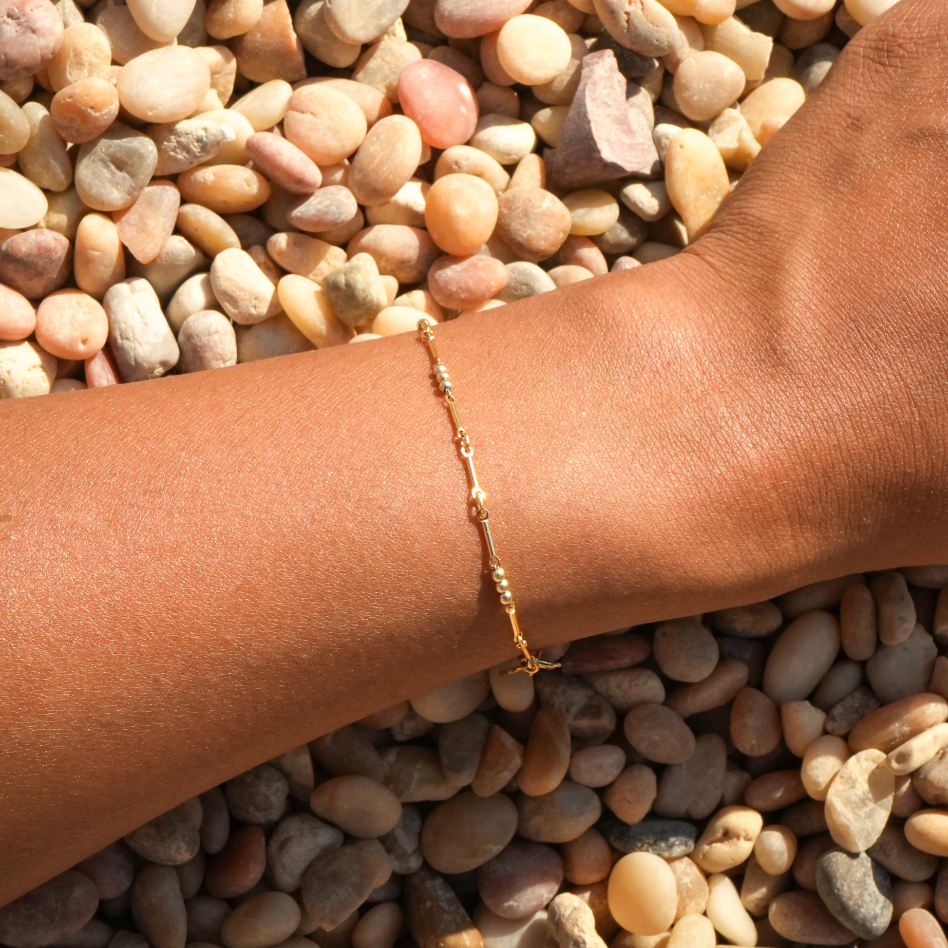 woman's wrist with gold-fill beaded bracelet on a bed of pebbles