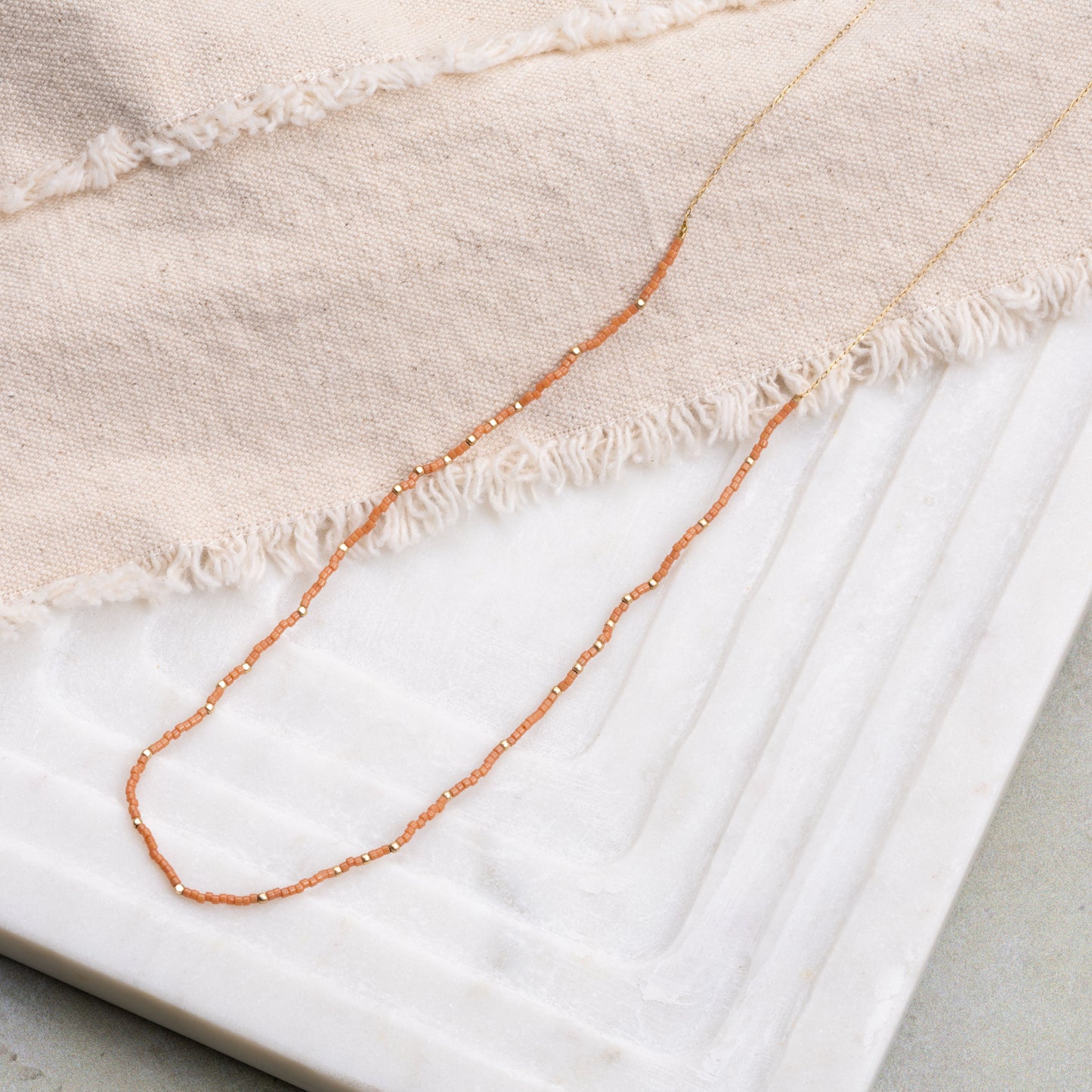 necklace with brown miyuki glass beads on a beige cloth and white tray